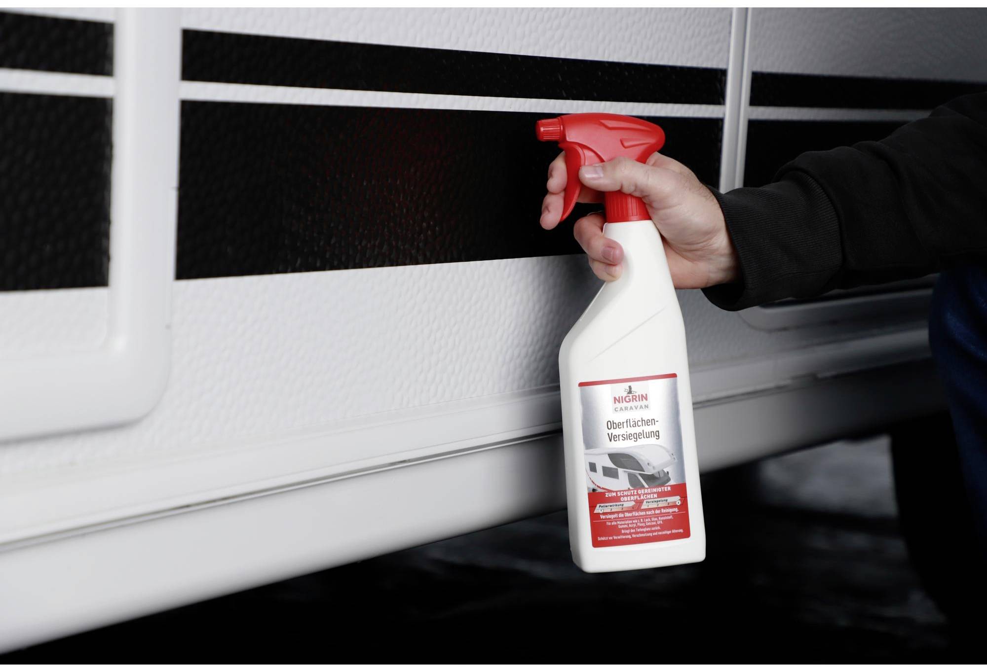 A hand is holding a white spray bottle with a red cap. The bottle is labelled 'Surface Sealing' and is being held against a white surface.