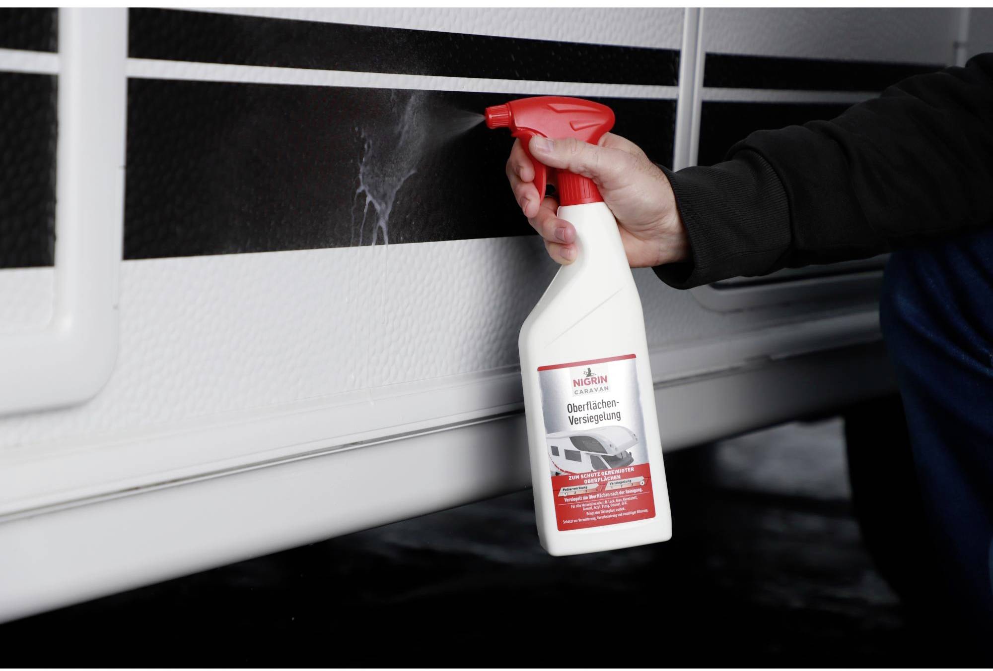 A hand holds a bottle of 'surface sealant' and is spraying the wall of a vehicle. A label is visible on the bottle.