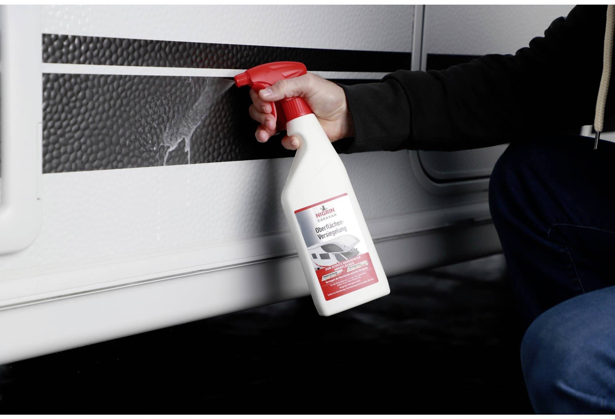 Hand holding cleaning bottle and spraying on caravan surface.