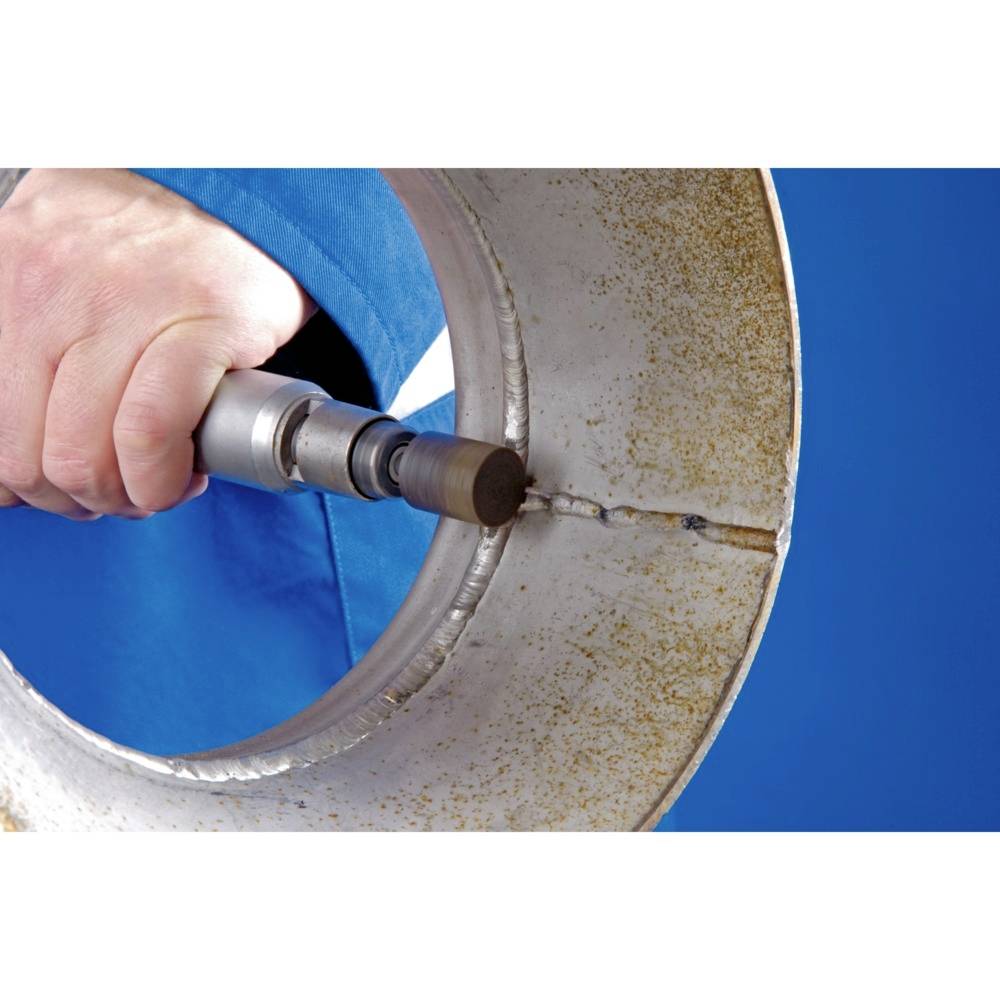 A hand is holding a tool to weld a crack in a large, metallic pipe. The person is wearing blue protective clothing.