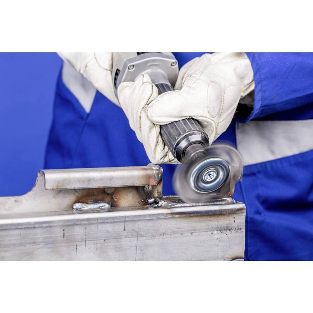 A person in blue workwear is grinding a metal edge with an angle grinder. Wearing gloves for safety.