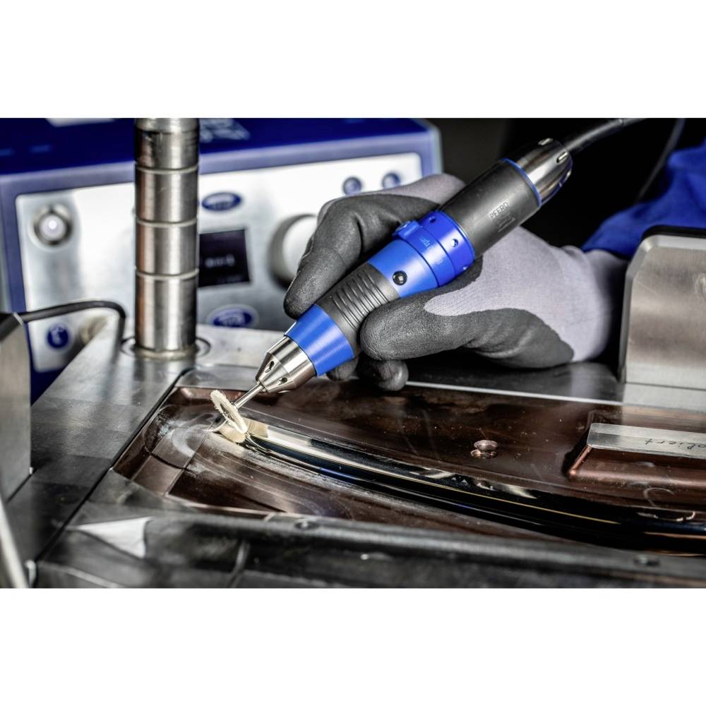 A person is using an electric precision tool to polish a metal surface in a workshop or industrial setting.