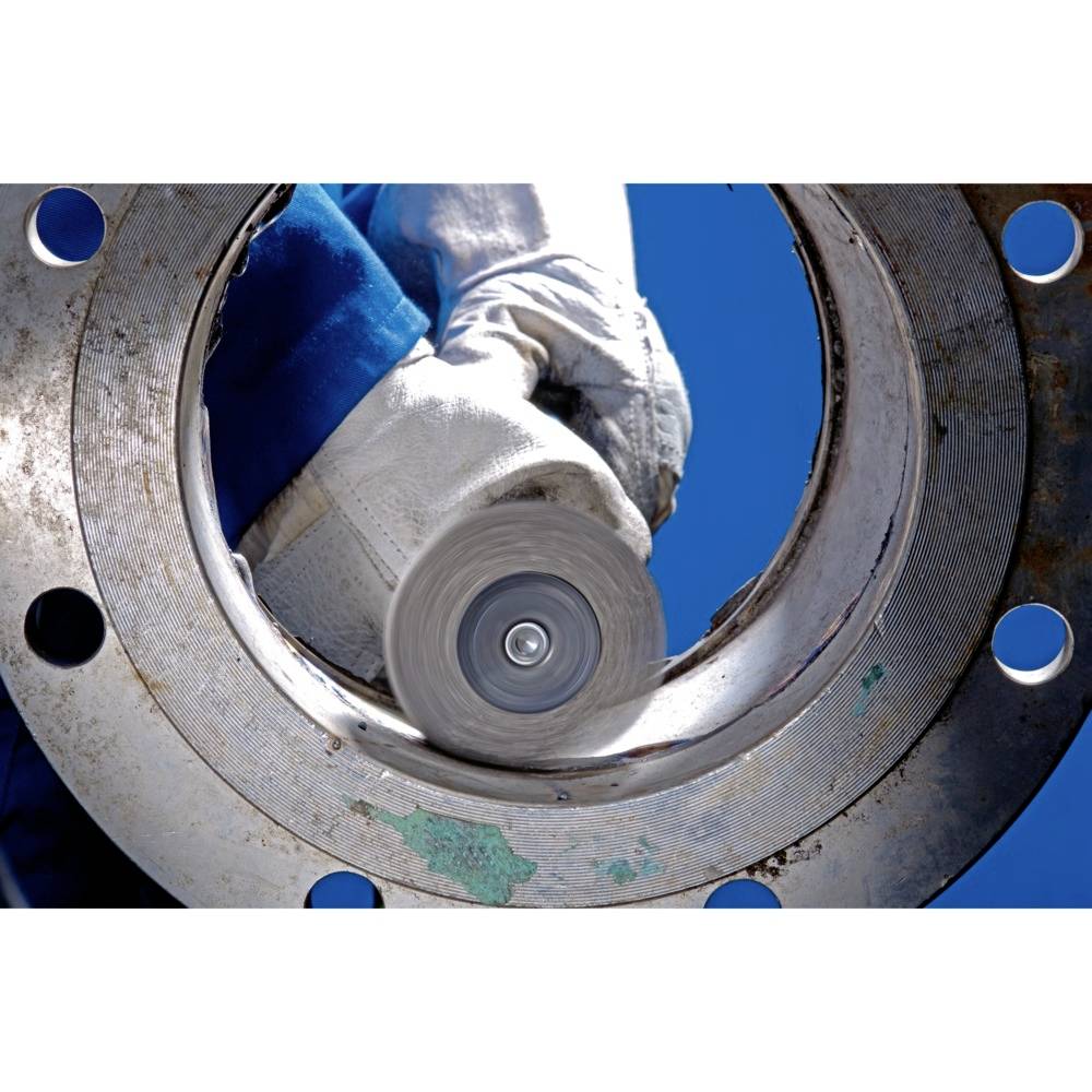 A worker in protective clothing is grinding the inner surface of a large metal flange with a grinding machine.