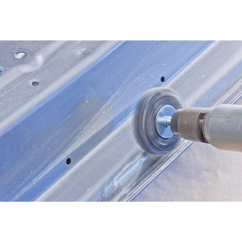 A person is polishing a blue metal sheet with a rotating tool to smooth and refine the surface.
