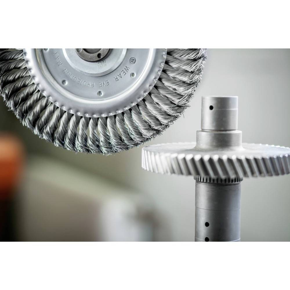 A polishing tool with a metal disc next to a gear shaft. Industrial setting with a focus on precision engineering.