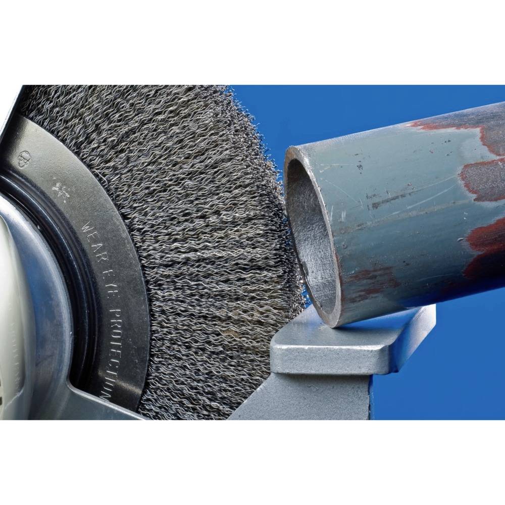 Metal is being worked on by a rotating wire brush. A pipe is being de-rusted, with details of the brush and pipe visible.
