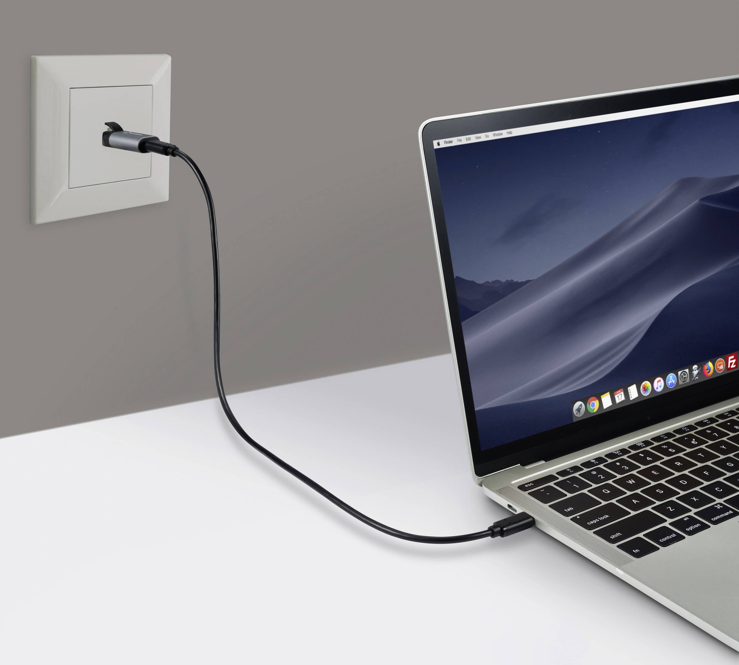 A laptop is plugged into a wall socket and displays the desktop screen. The background image shows a mountain landscape.