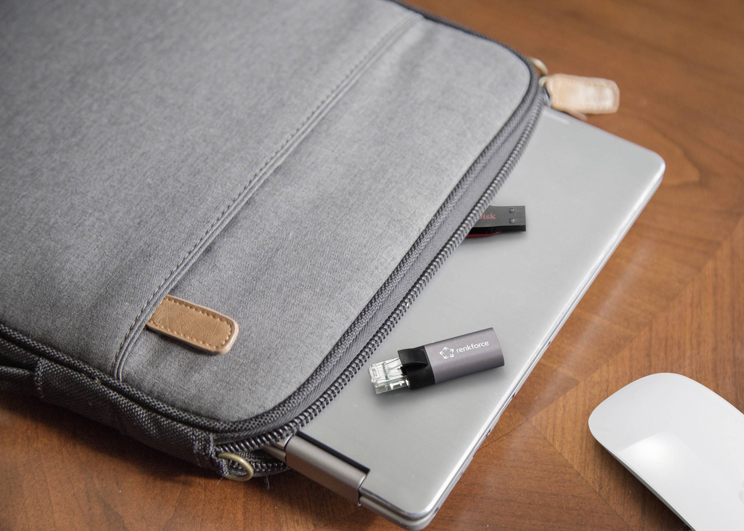 A grey laptop protrudes halfway from a grey fabric bag on a wooden table. Two USB drives lie beside the laptop.