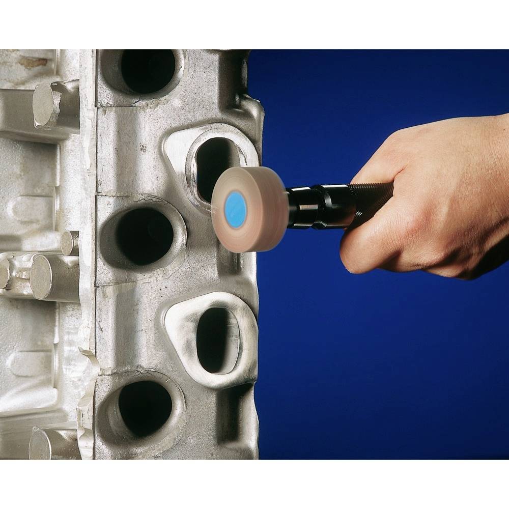 A hand carefully holds a rotating tool and is machining the surface of a metallic engineering component.