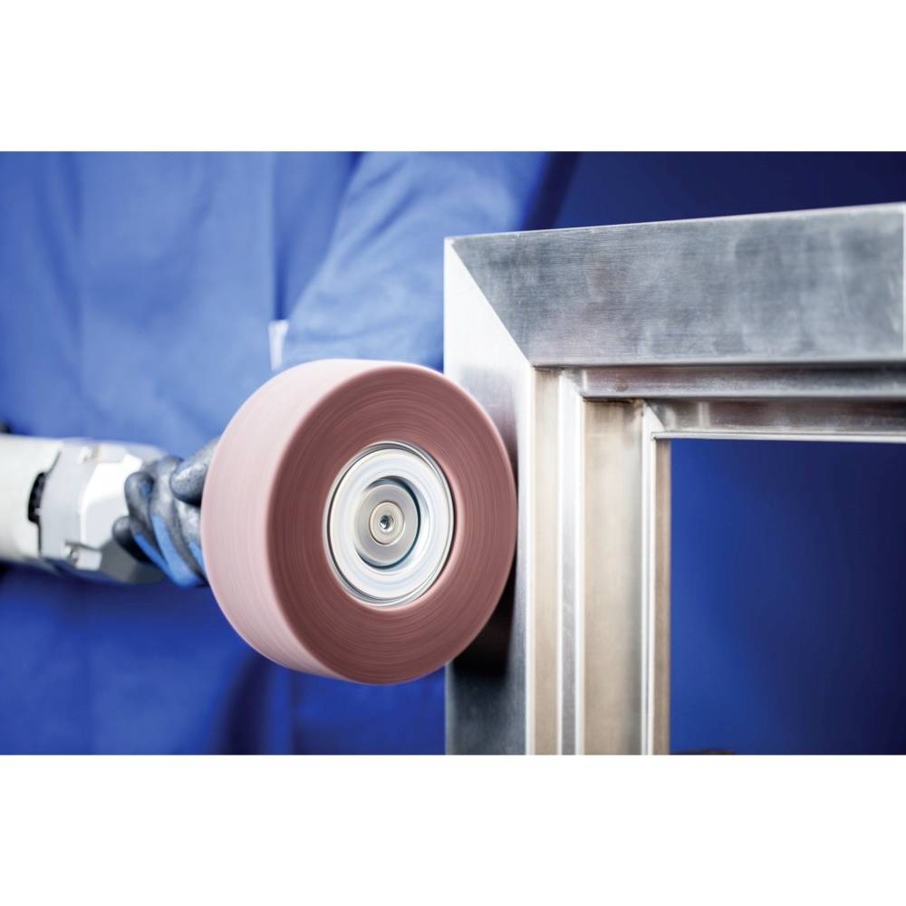 A person in blue protective clothing is polishing a metal frame with a rotating polishing disc.