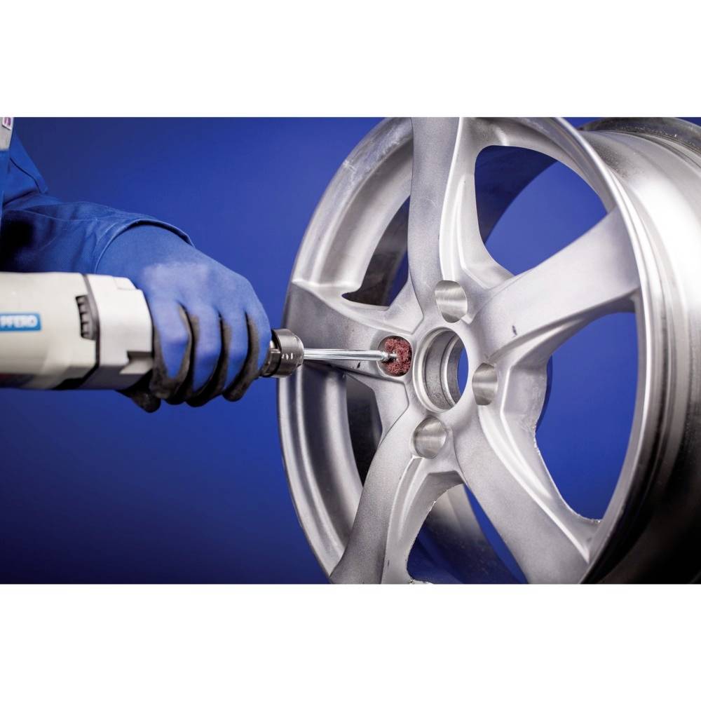 A person wearing blue gloves is repairing a silver car wheel with a tool against a blue background.