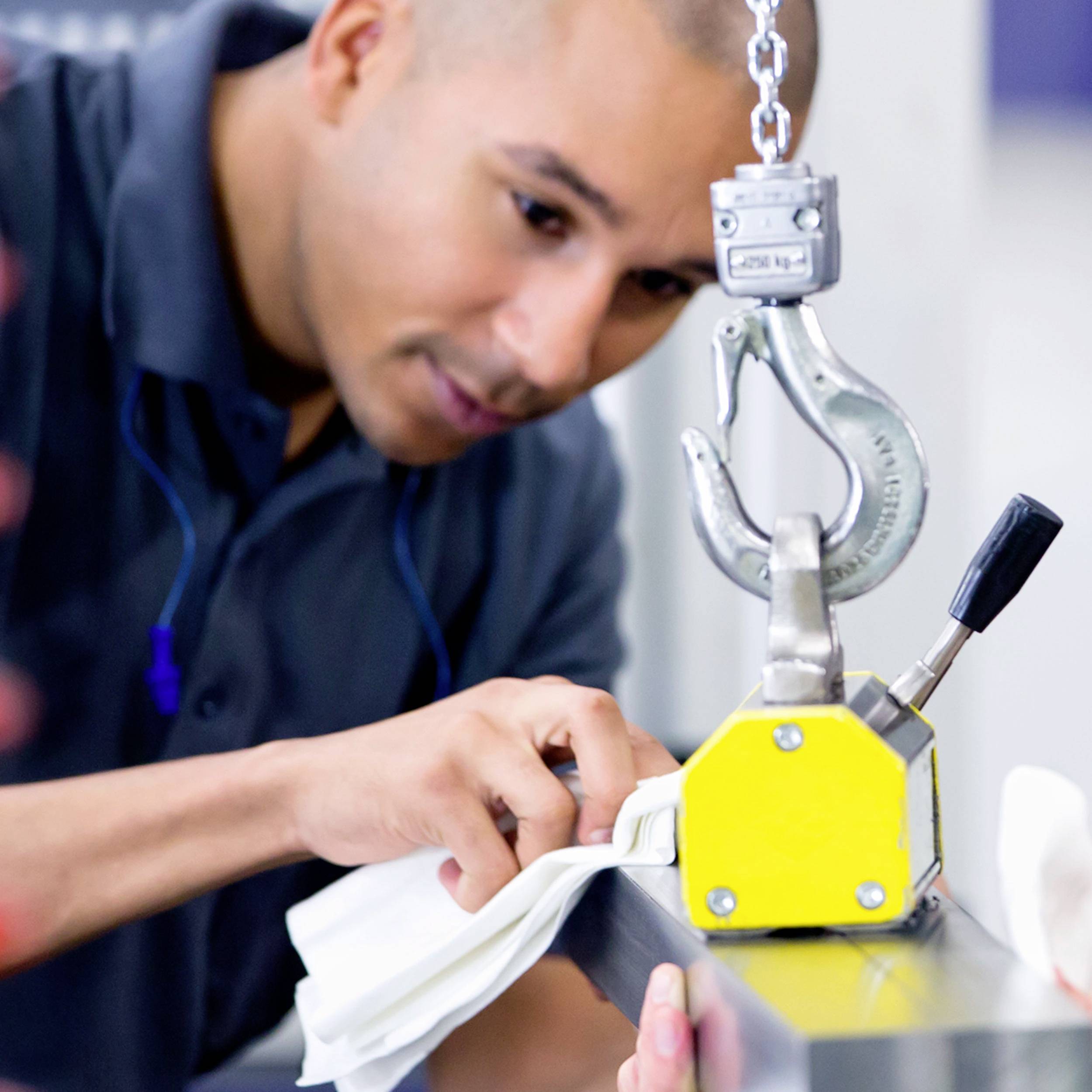 A person is carefully inspecting a yellow machine component, closely examining a raised metal part with a hook.