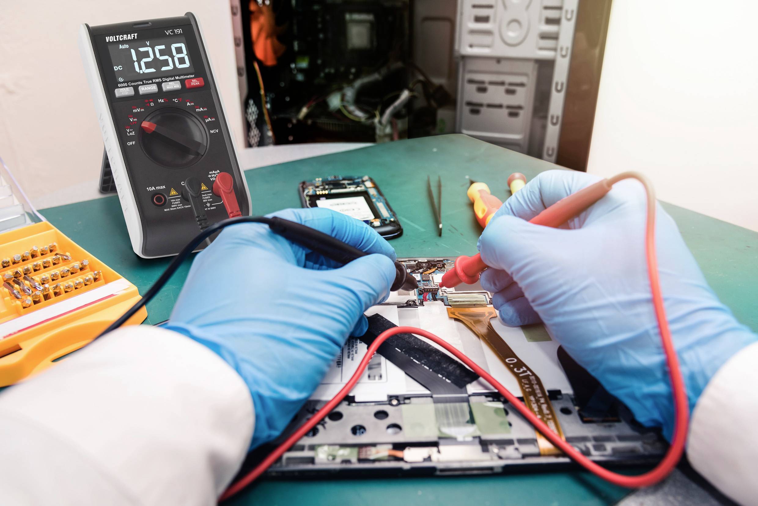 A person wearing blue gloves is repairing an electronic device using a multimeter. Tools are visible in the background.
