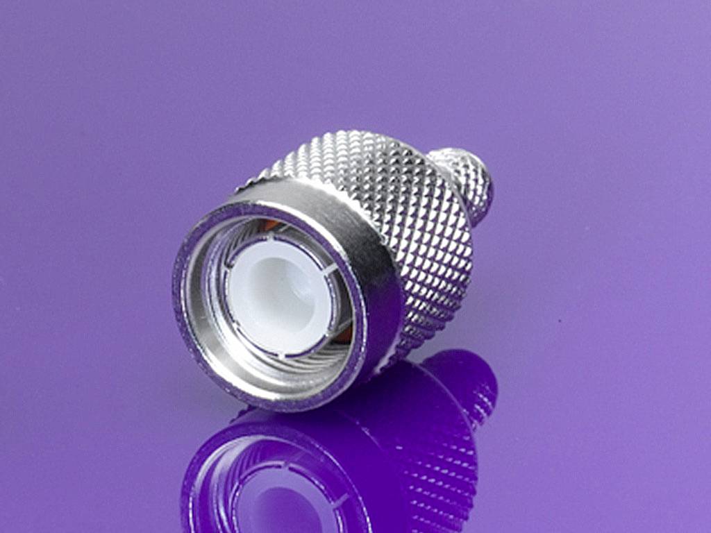 Metal adapter on a purple background, showing a coaxial plug with a ridged surface and reflected light.