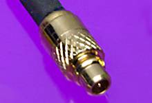 A golden coaxial plug on a black cable against a lilac background.