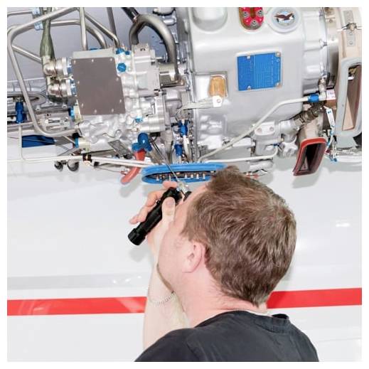 Ein Techniker inspiziert einen Flugzeugtriebwerk unter einem Flügel mit einer Taschenlampe und überprüft die freiliegende Maschinen und Schläuche.