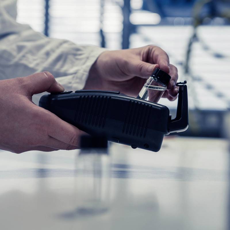 A freehand holder presenting a glass bottle next to a device in a laboratory environment, illustrating experimental analysis or research.