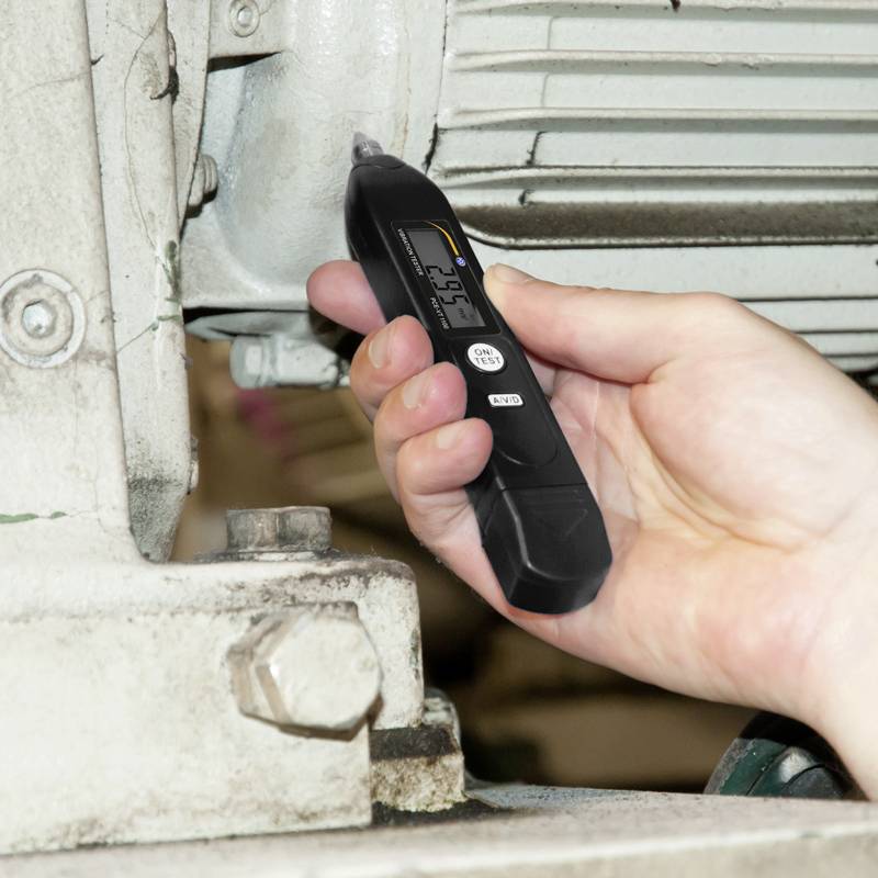 A hand is holding a portable device against a metal surface, with the device displaying '9.75' on the screen.