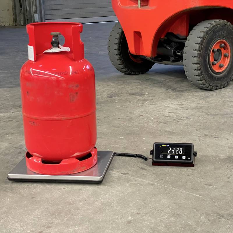 Red propane gas cylinder stands on a weighing scale next to a forklift. The display shows the weight of the cylinder as 23.28 kg.