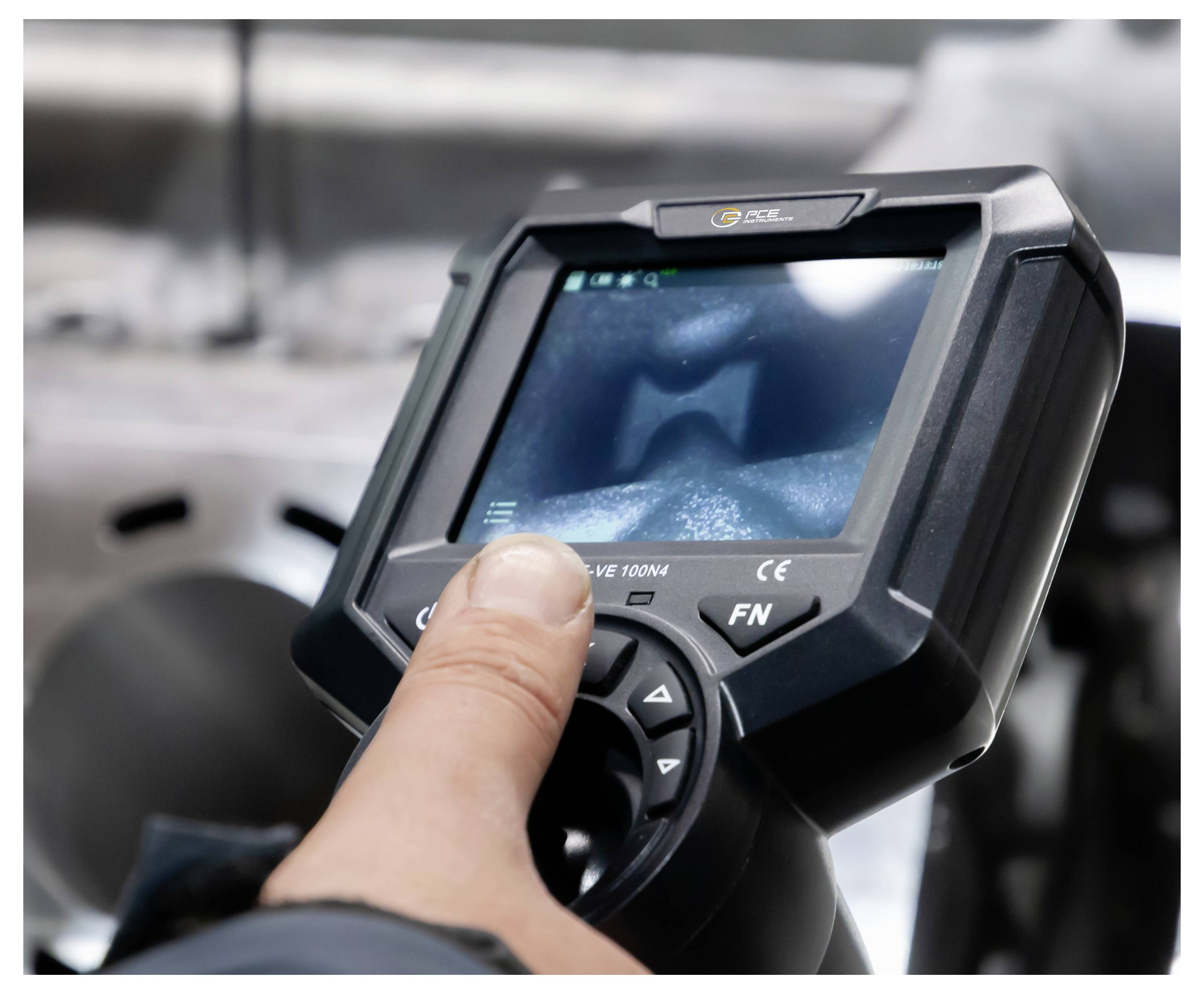 Person drückt Tasten auf einem tragbaren industriellen Gerät mit einem Bildschirm, wahrscheinlich ein Scanner oder Controller, in einer Werkstattumgebung