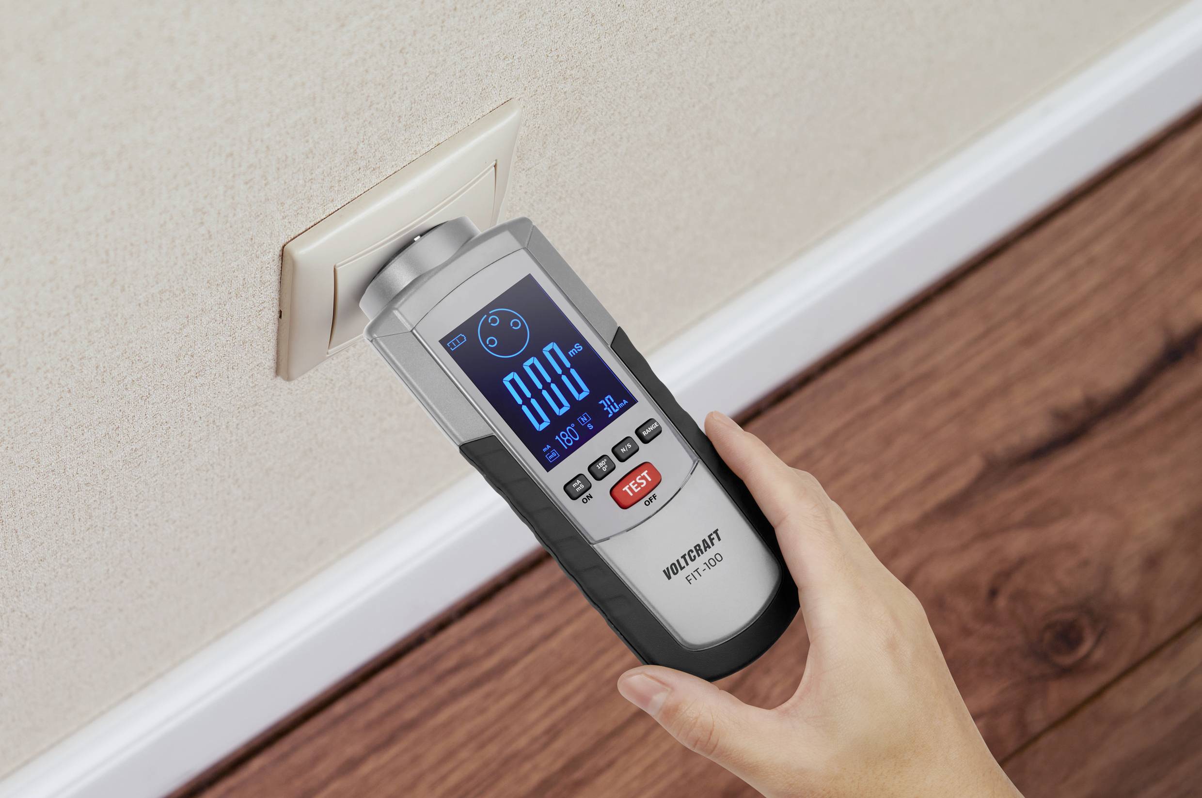 A person is holding an electrical measuring device against a power socket to check the voltage. The display shows 0.00.