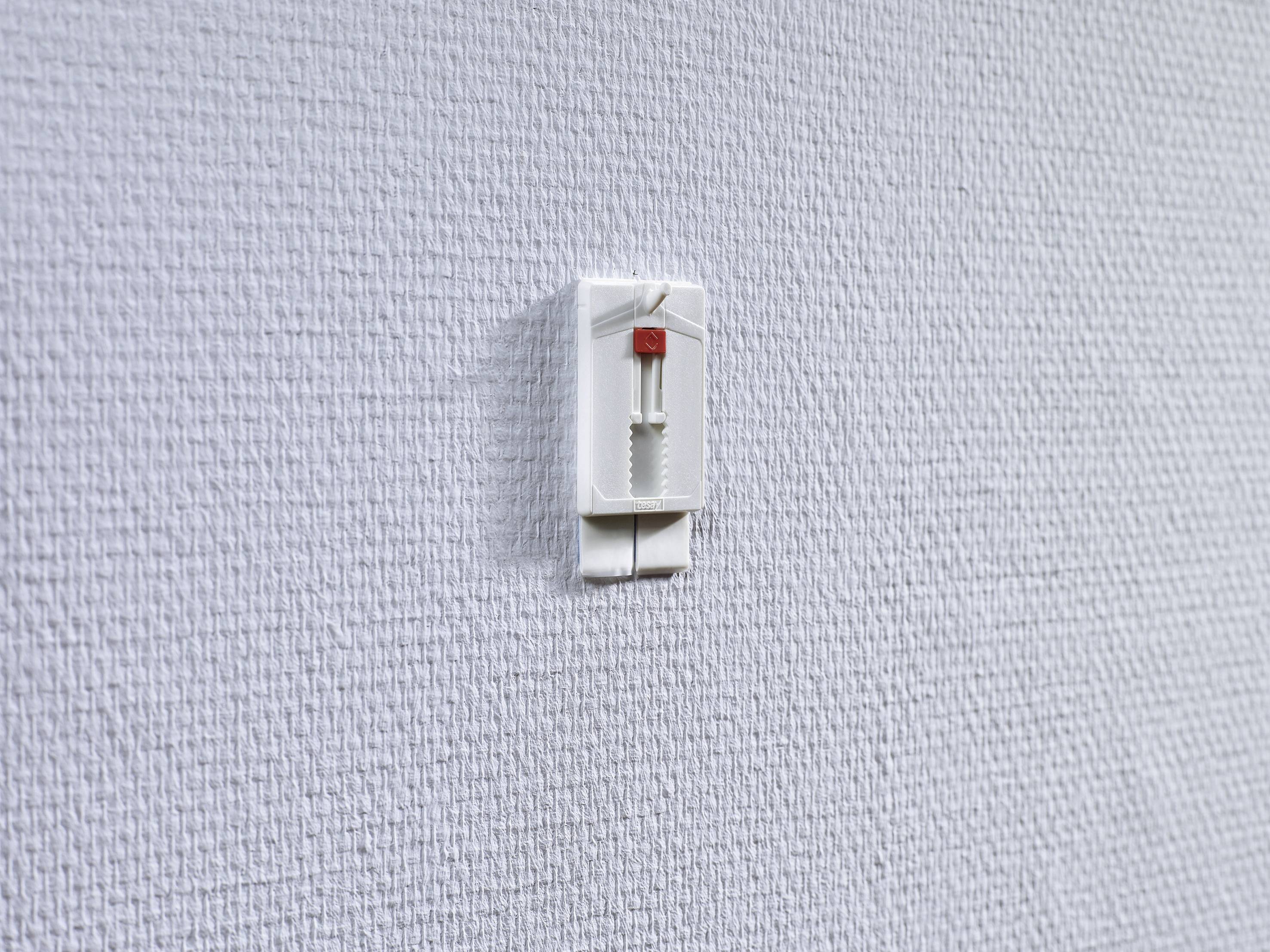A white wall hook on a textured white wall, with nothing hanging on it.