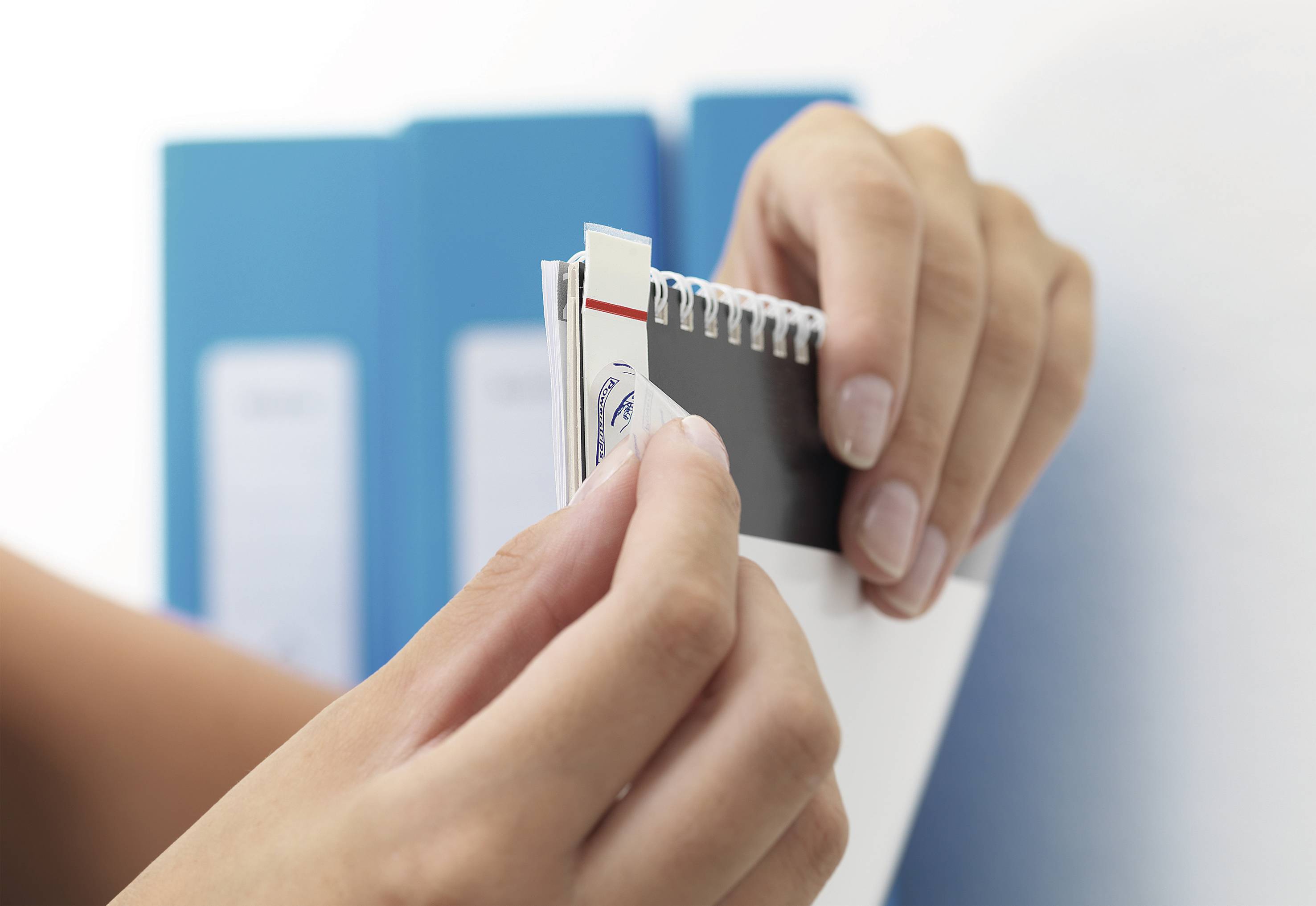 A person is flicking through a colour sampler in front of blue folders. A colour sample is being pulled out.