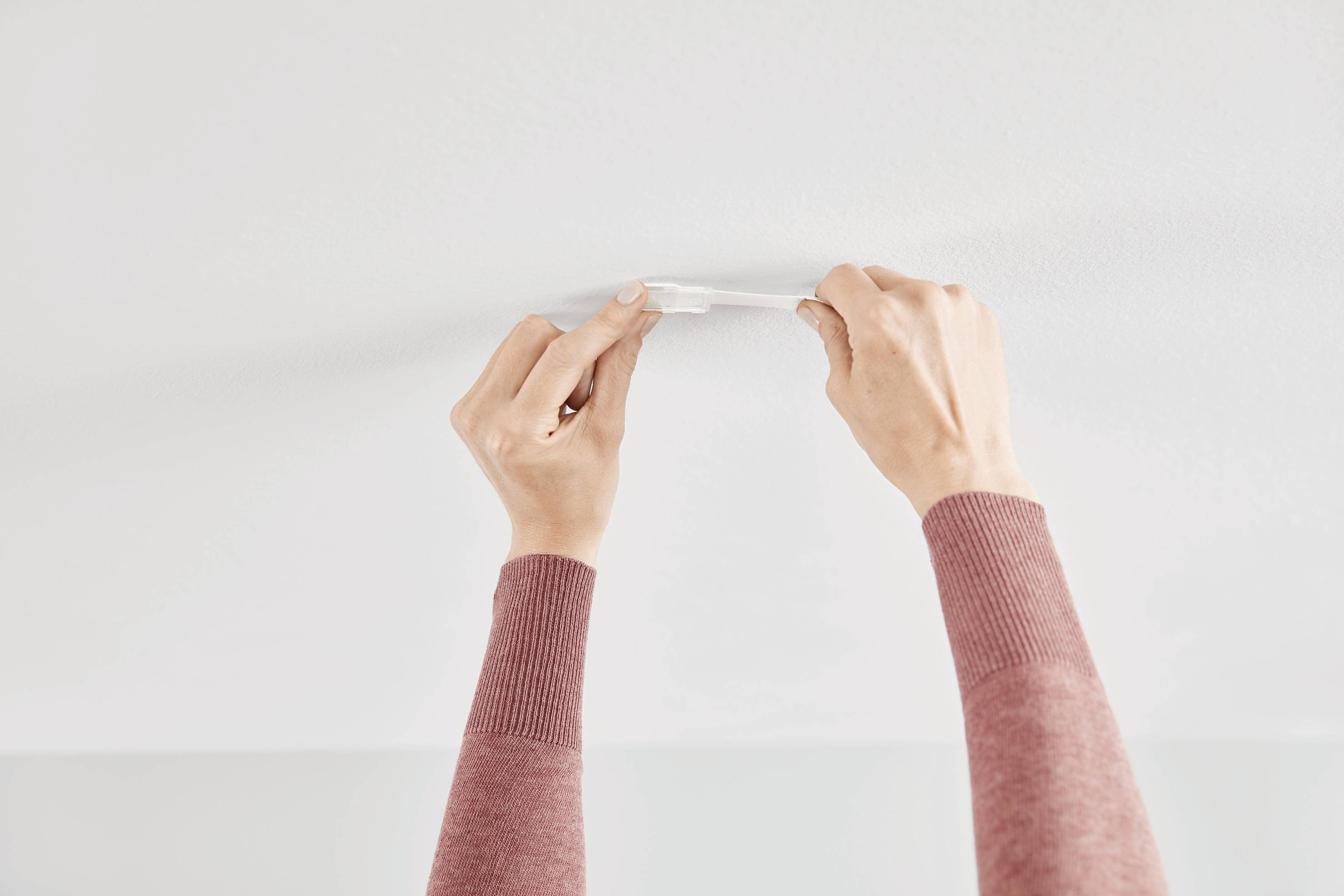 Hands of a person installing a smoke detector on a ceiling.