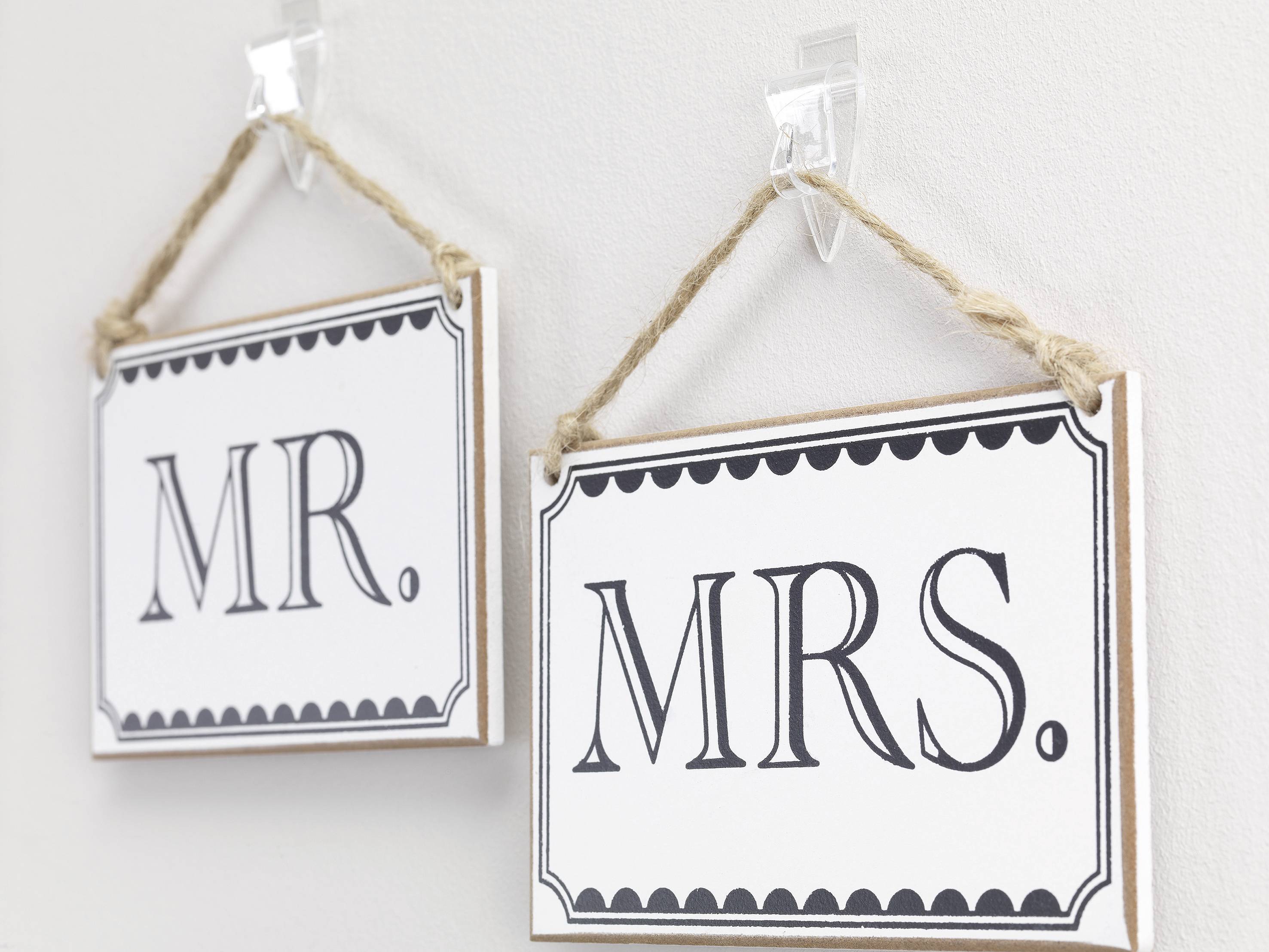 Two signs on the wall with the inscriptions 'Mr.' and 'Mrs.', hung on transparent hooks using ropes.