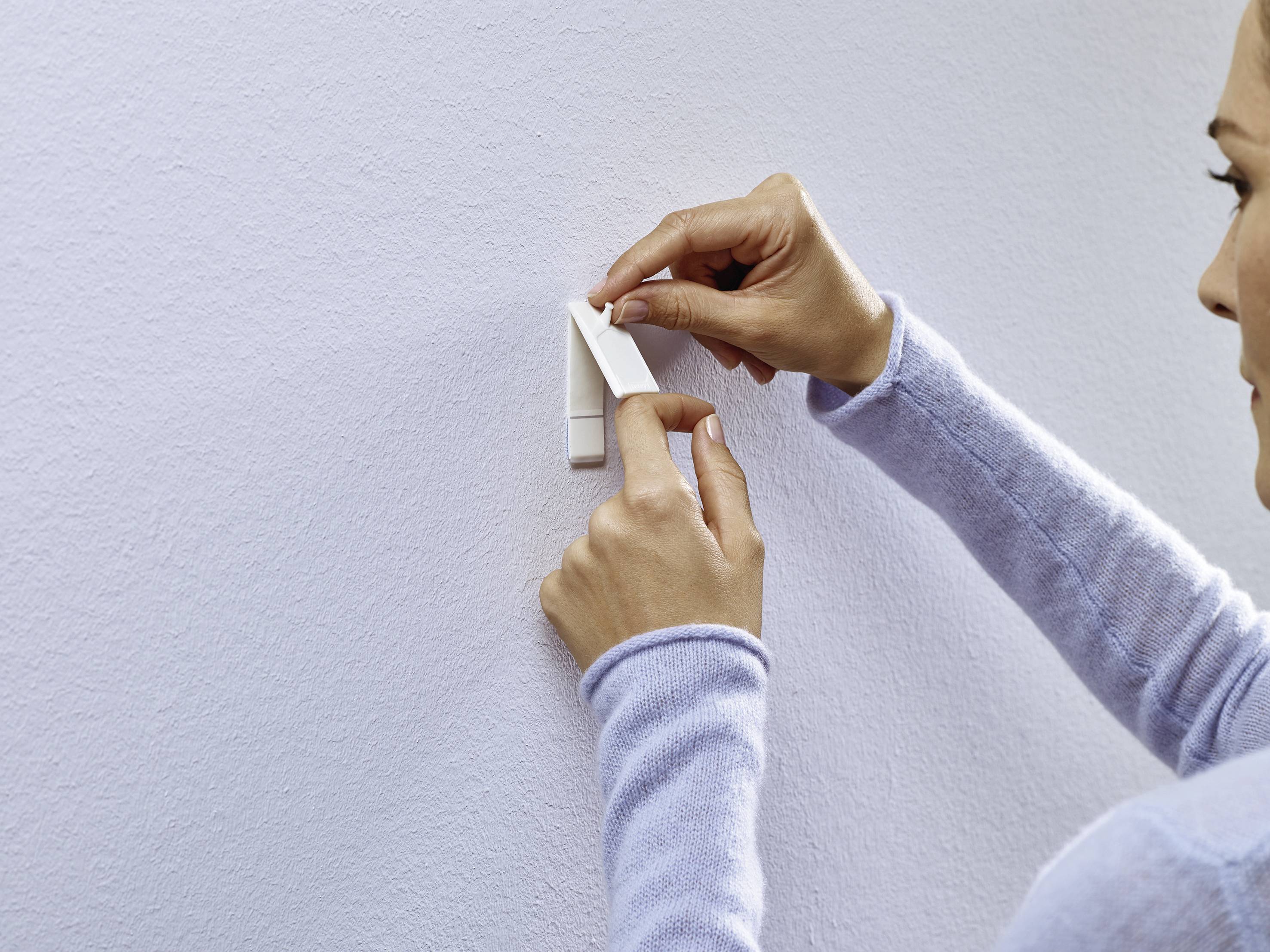 A person is attaching a strip of tape to a white wall. They are wearing a light blue jumper.