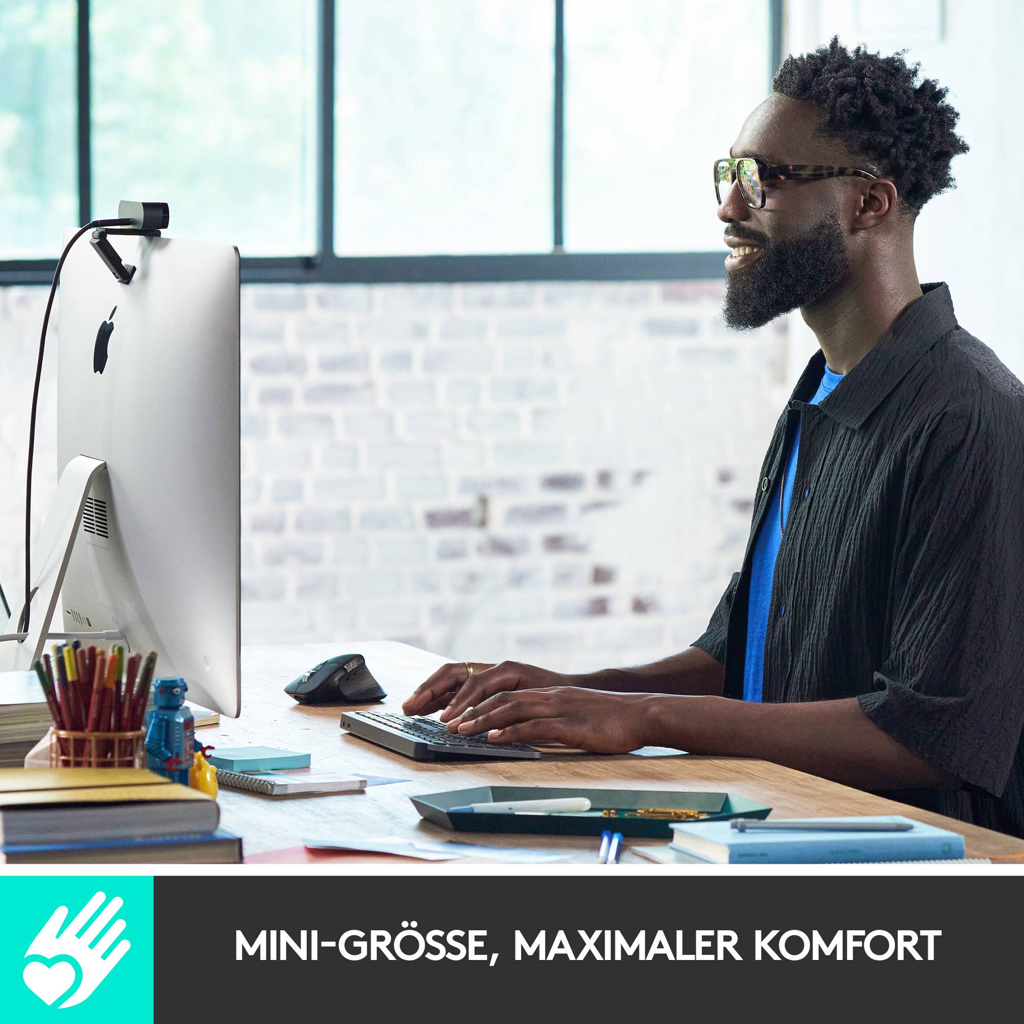 A man sits smiling in front of a computer screen, typing on the keyboard. In the foreground, it reads 'Mini-size, maximum comfort'.