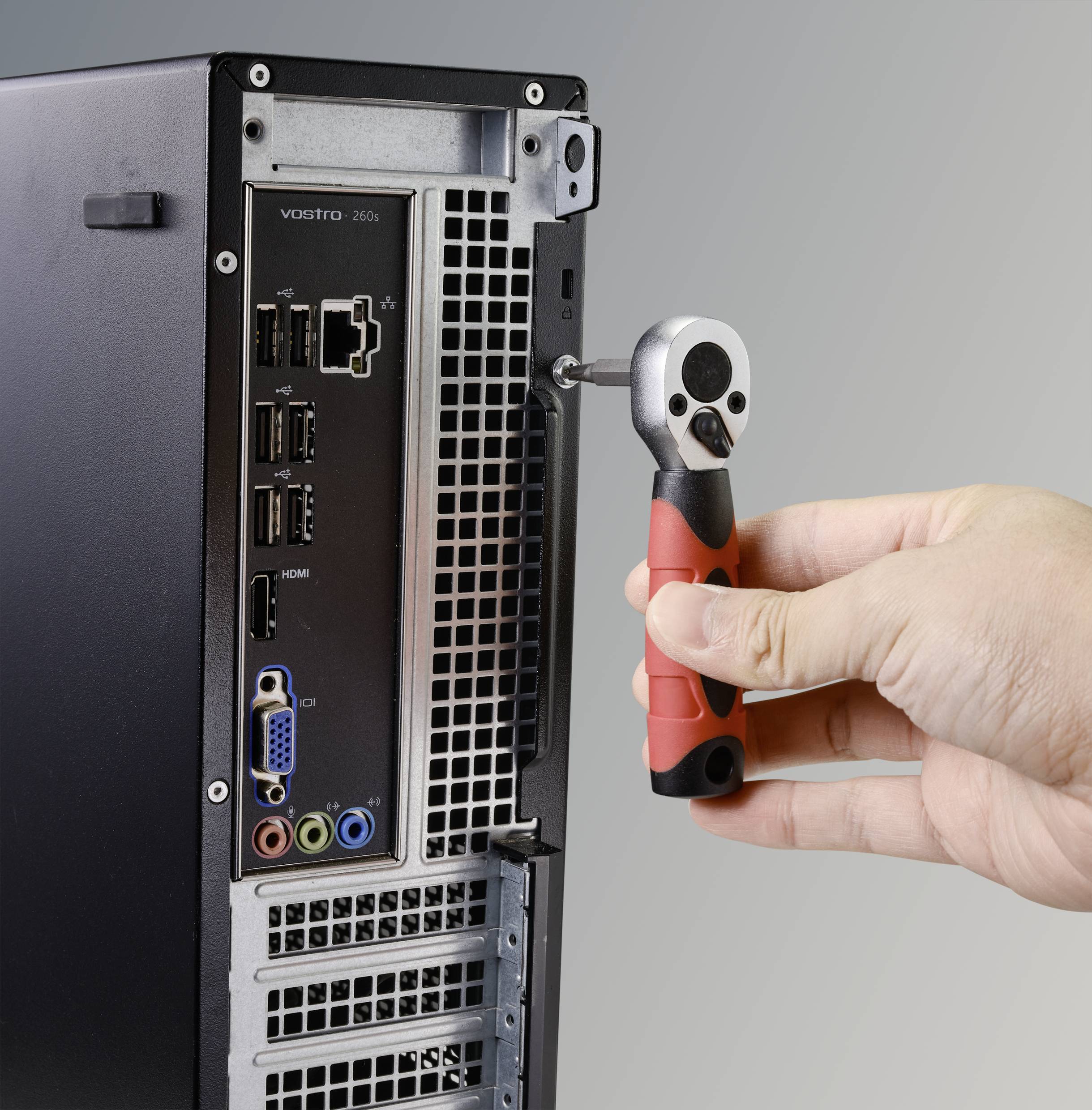 A hand is using a screwdriver to open the back of a computer case. Various ports are visible.