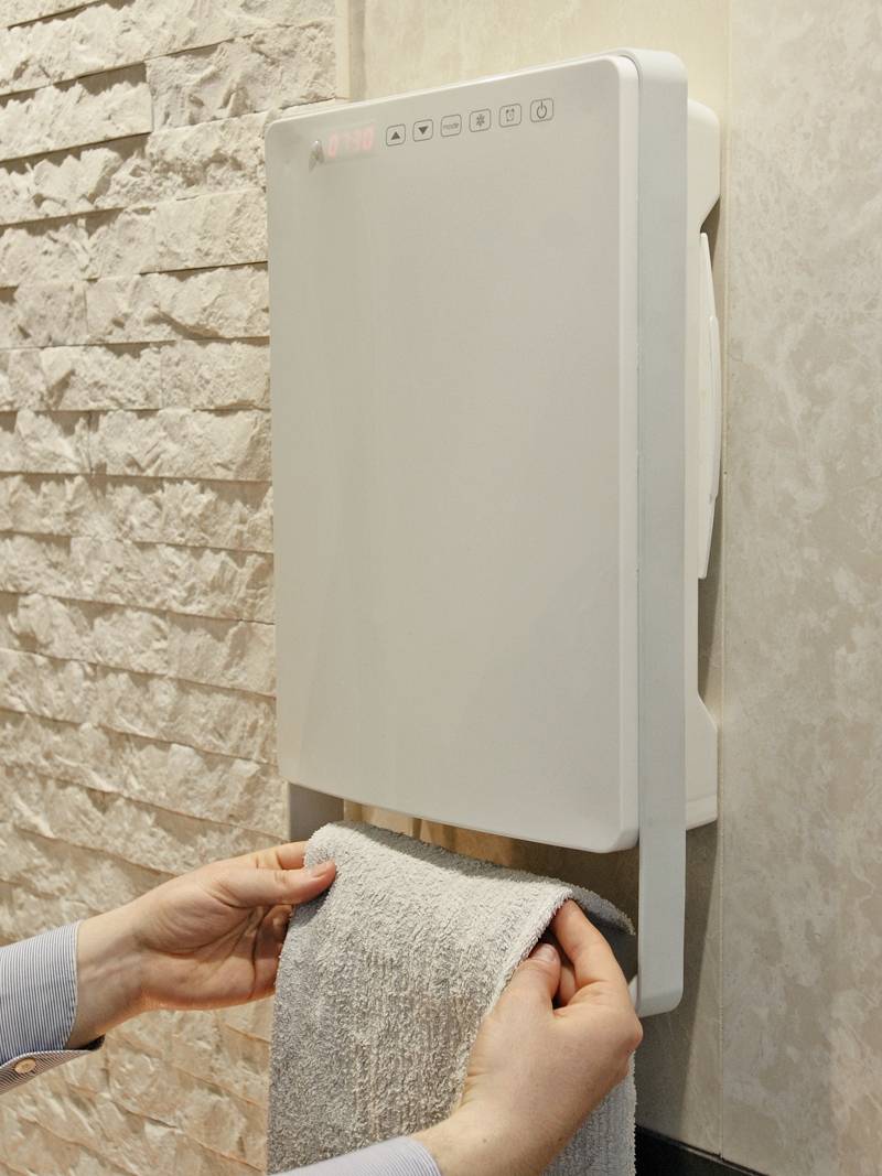 A hand dryer blows air onto a towel held by a person. The dryer is mounted on a brick wall.