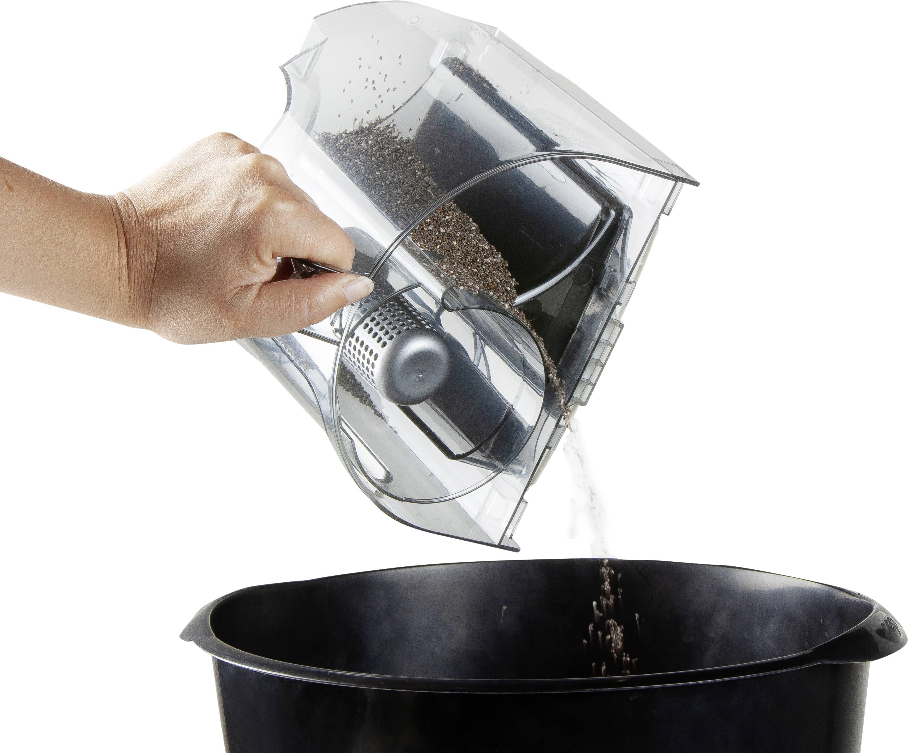 A hand empties a container of dust and dirt into a black rubbish bin.