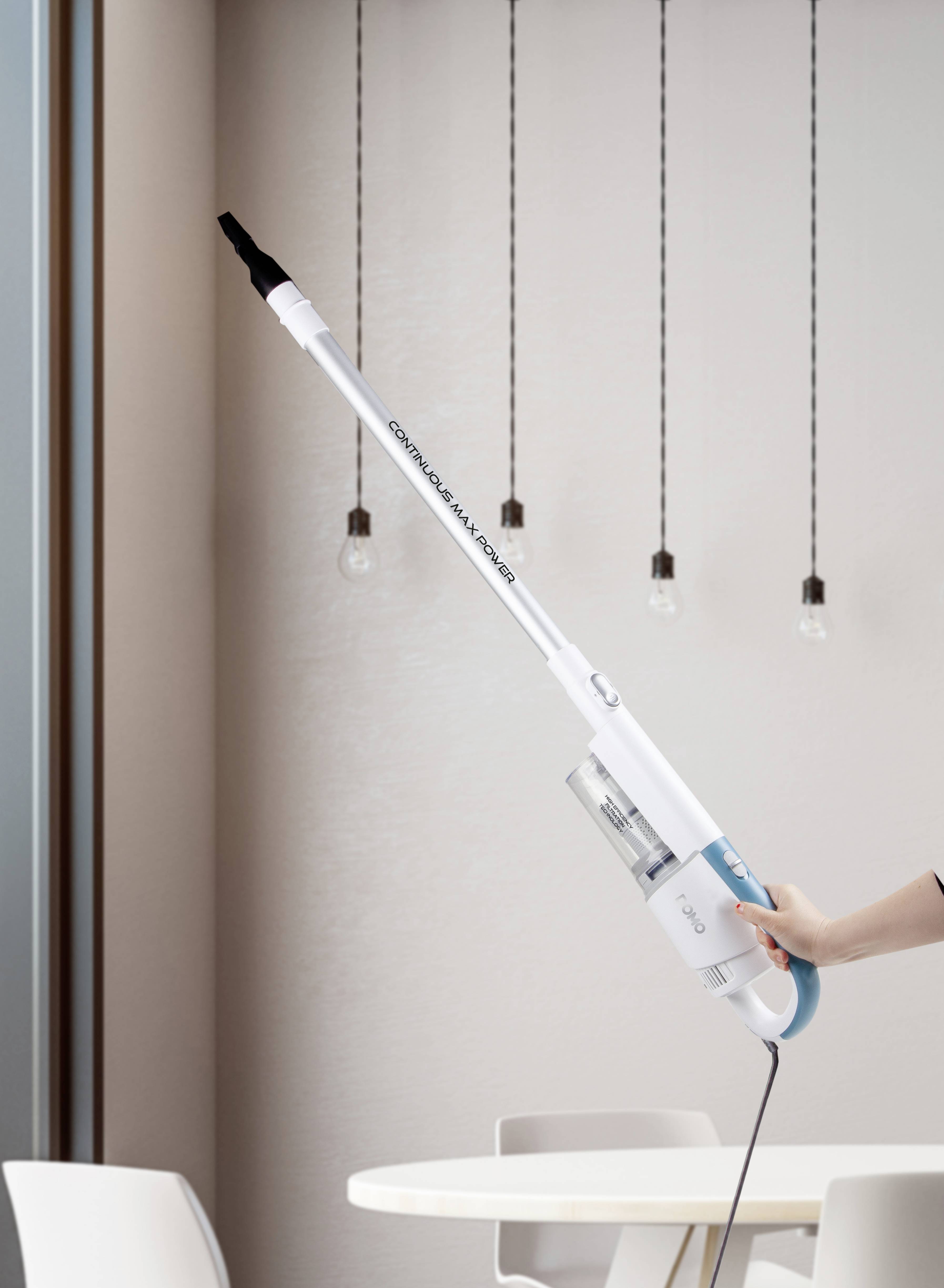 A hand is holding a lightweight, cordless vacuum cleaner standing upright, with a modern living room background and hanging lamps.
