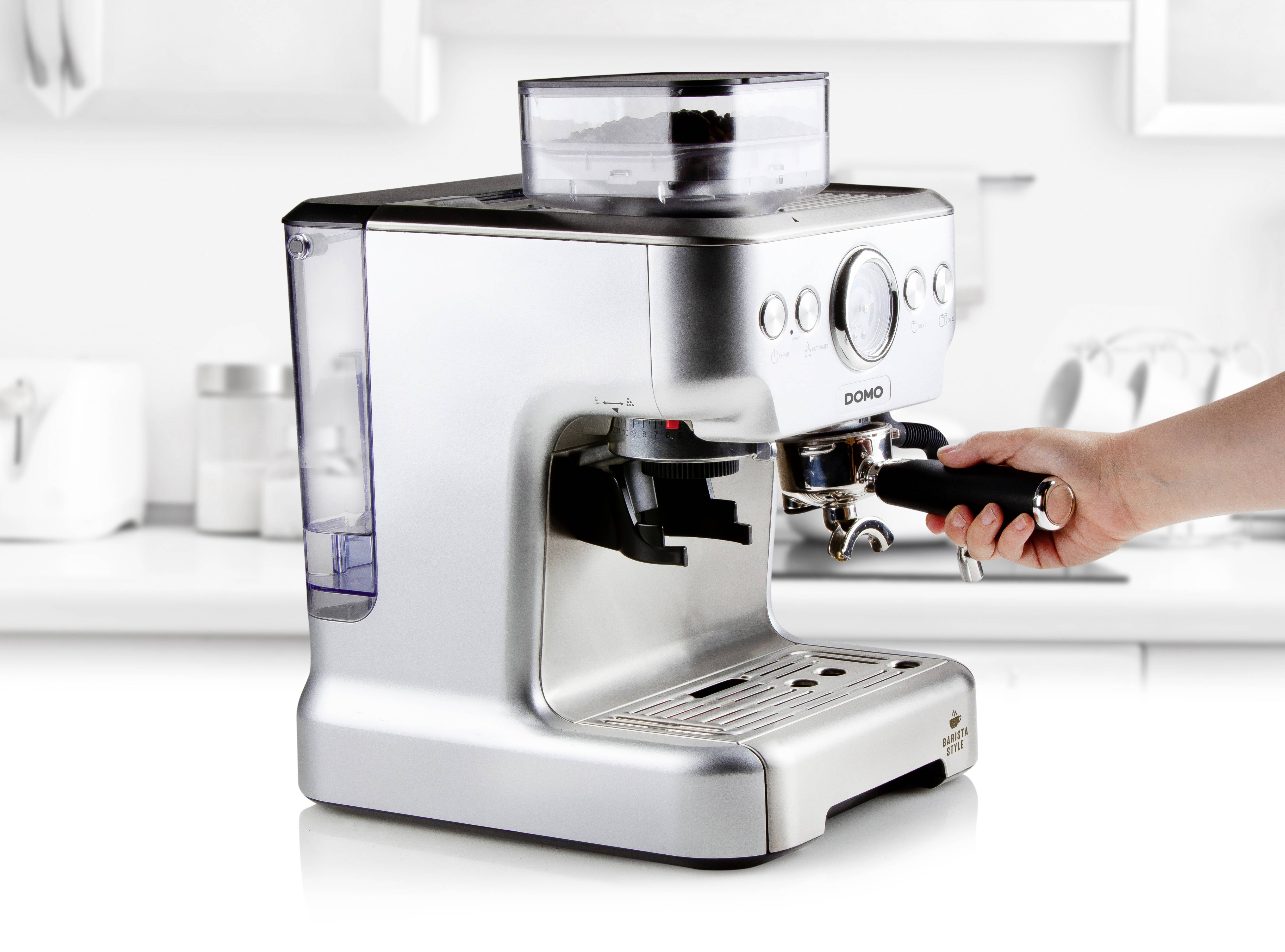 Silver espresso machine in a contemporary kitchen, a hand holding the portafilter.