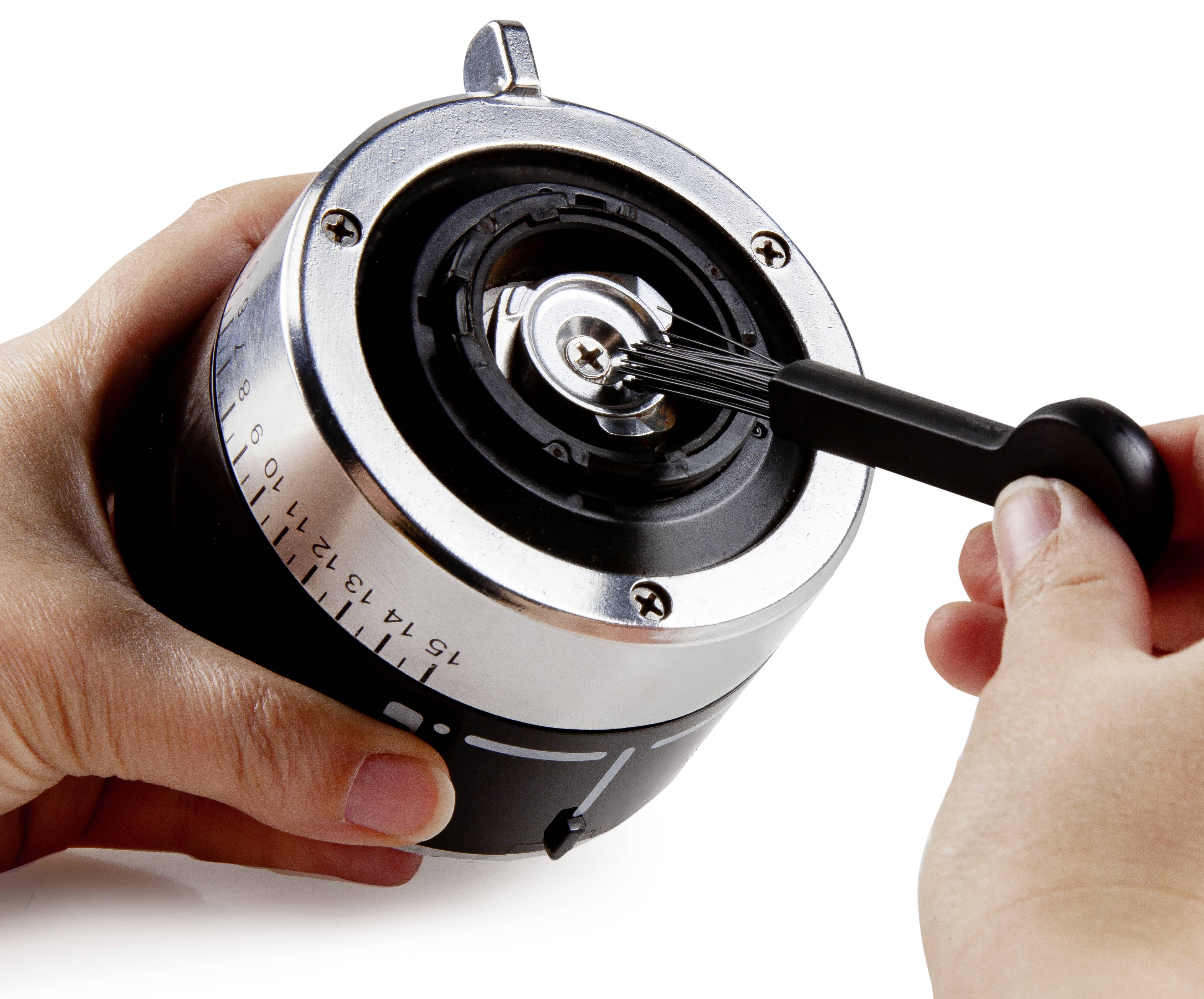 A person is holding a coffee bean grinder and adjusting the grind size setting with a small lever or screwdriver.