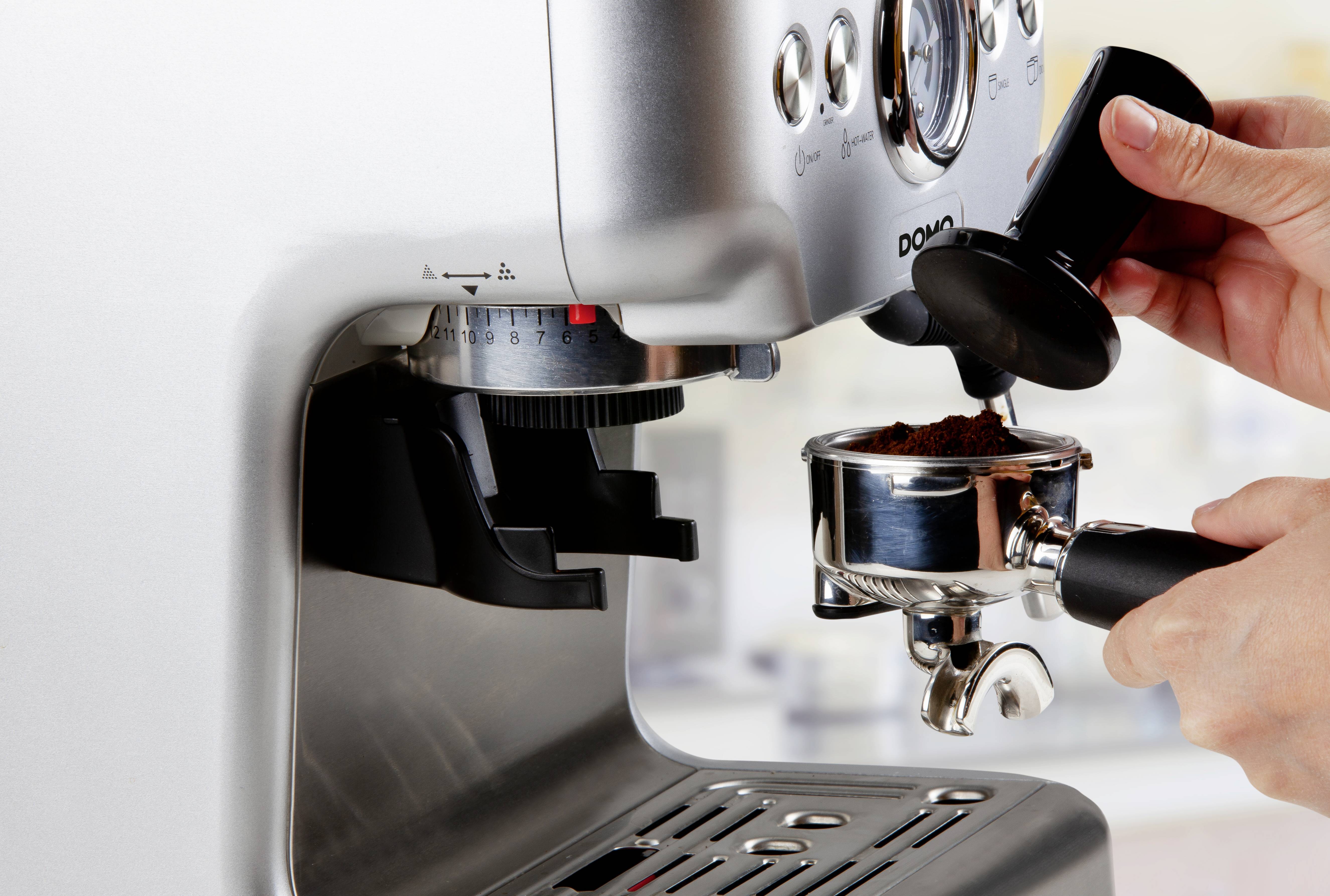 A person is grinding coffee for an espresso machine's portafilter.