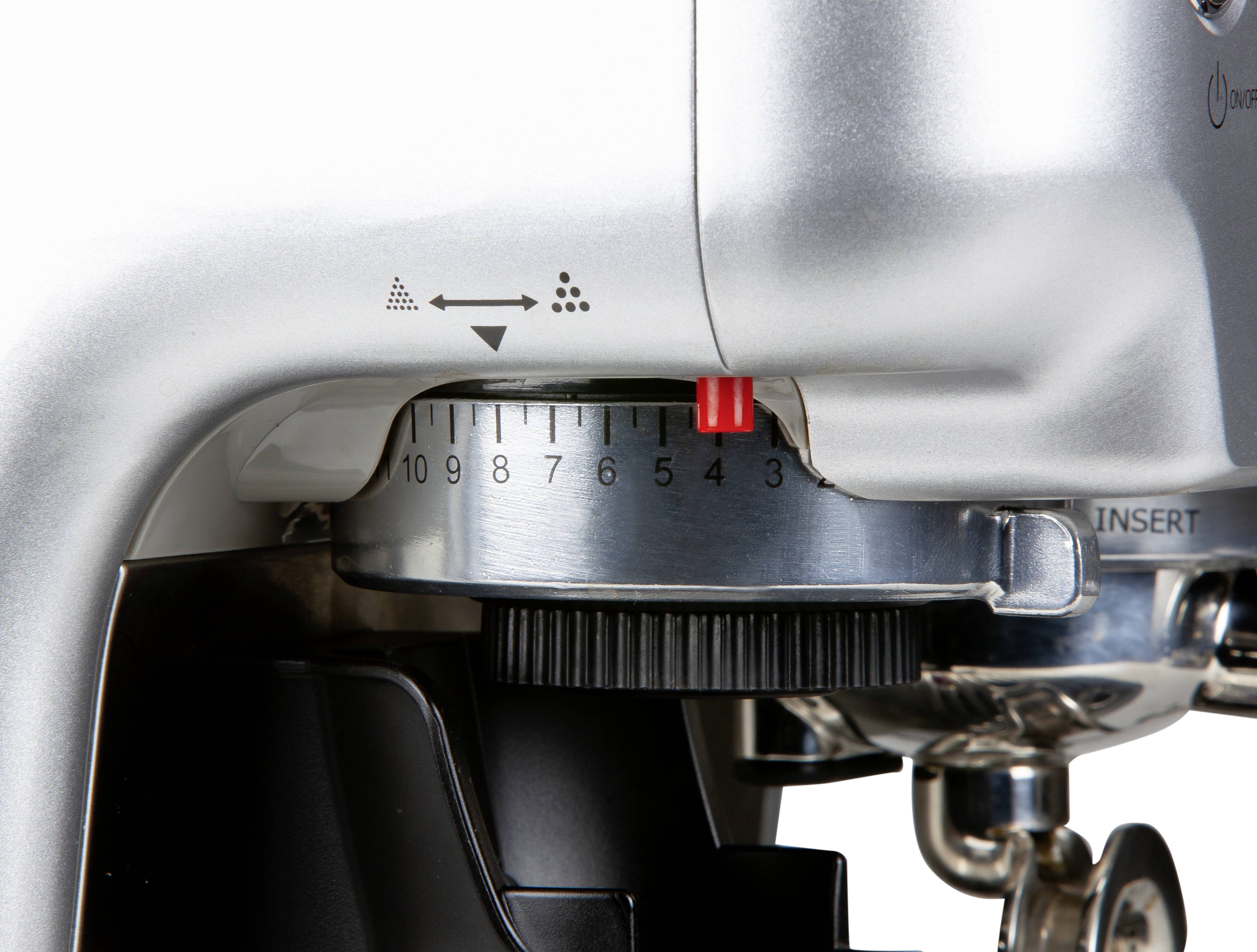 Close-up of a coffee machine, showing the grind size adjuster with a scale from 0 to 10 and a red marker at 5.