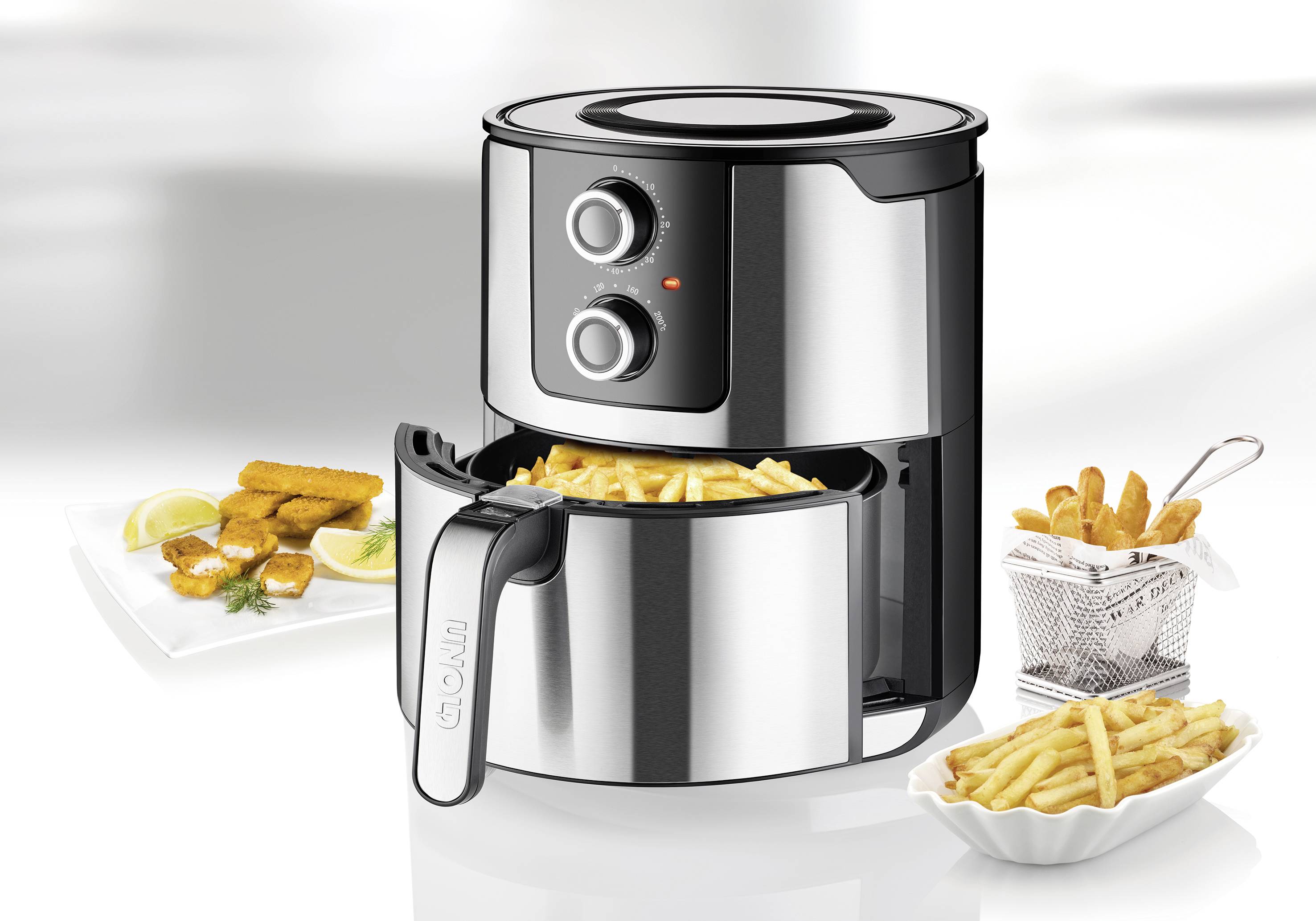 Silver air fryer with an open drawer filled with chips. Beside it, a plate with crispy nibbles and lemon wedges.