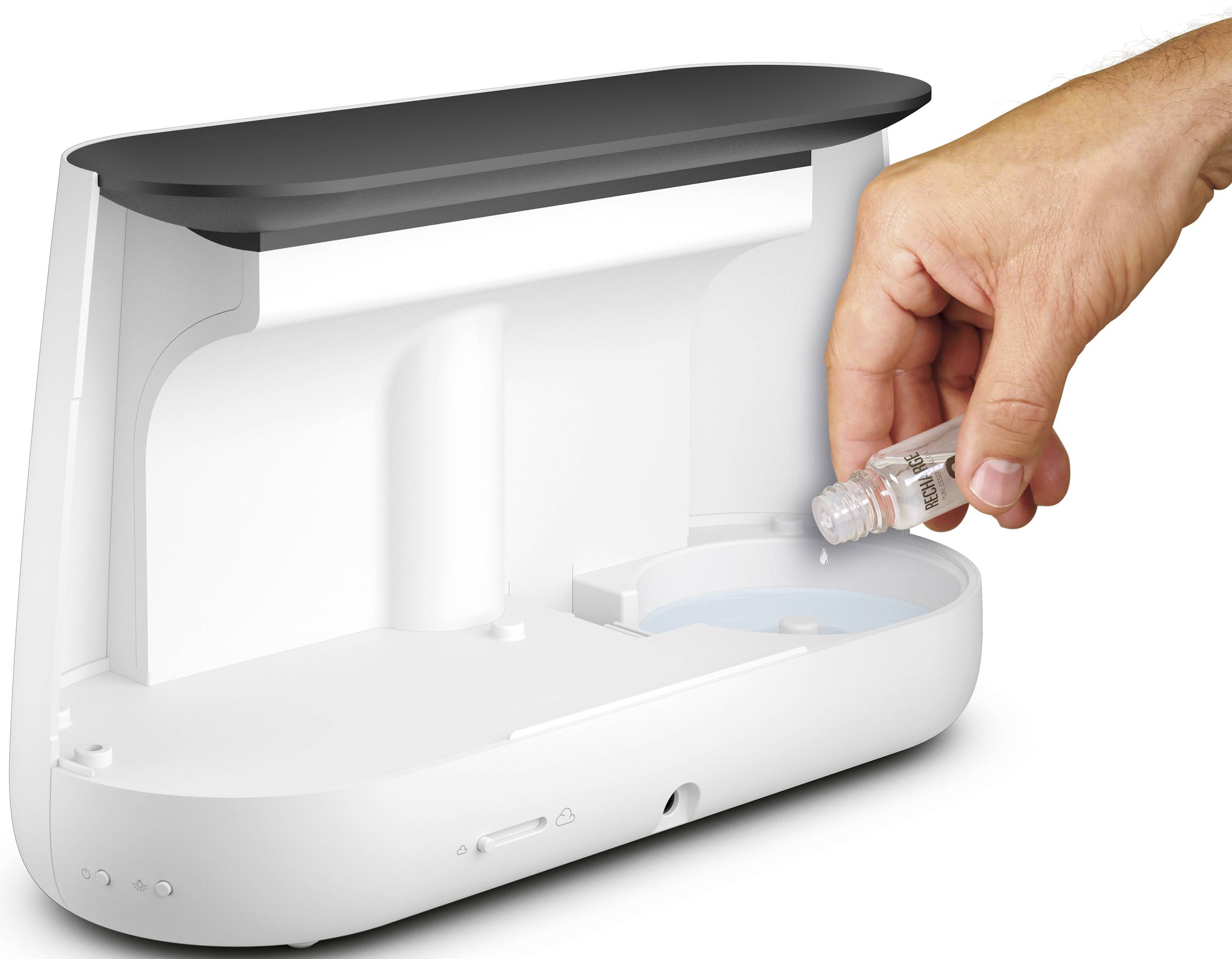 A hand is holding a small liquid container and pointing it towards a white, open device that appears to be a humidifier.