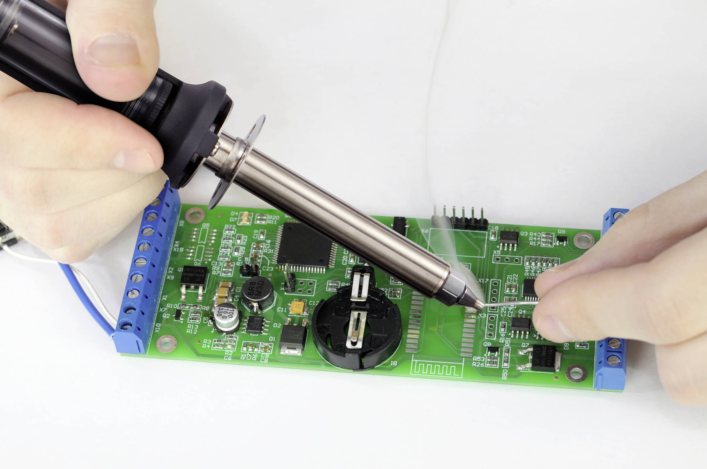 Someone is soldering a green circuit board.