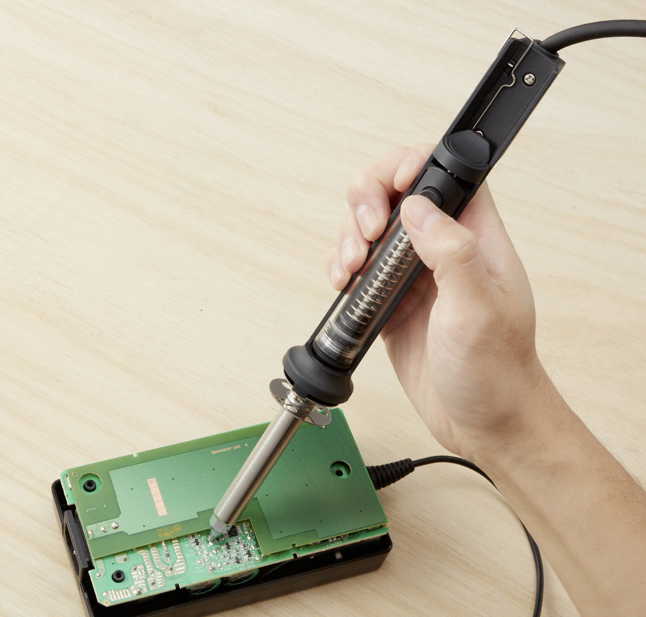 A person is soldering with a soldering iron on a circuit board. The iron is touching the board while the hand stabilises it.