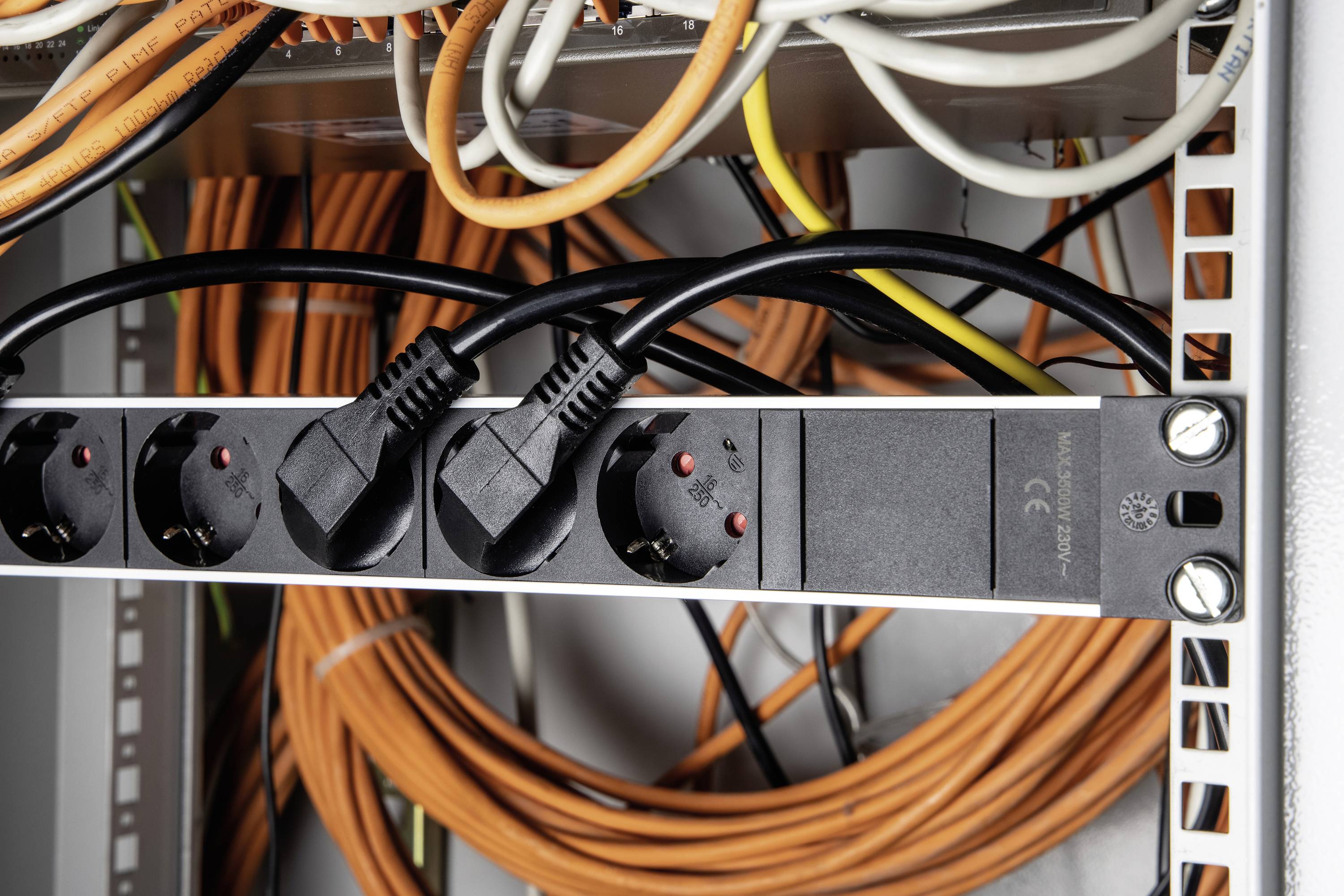 A network cabinet with several orange and black cables connected to power strips. Focus on cable connections.