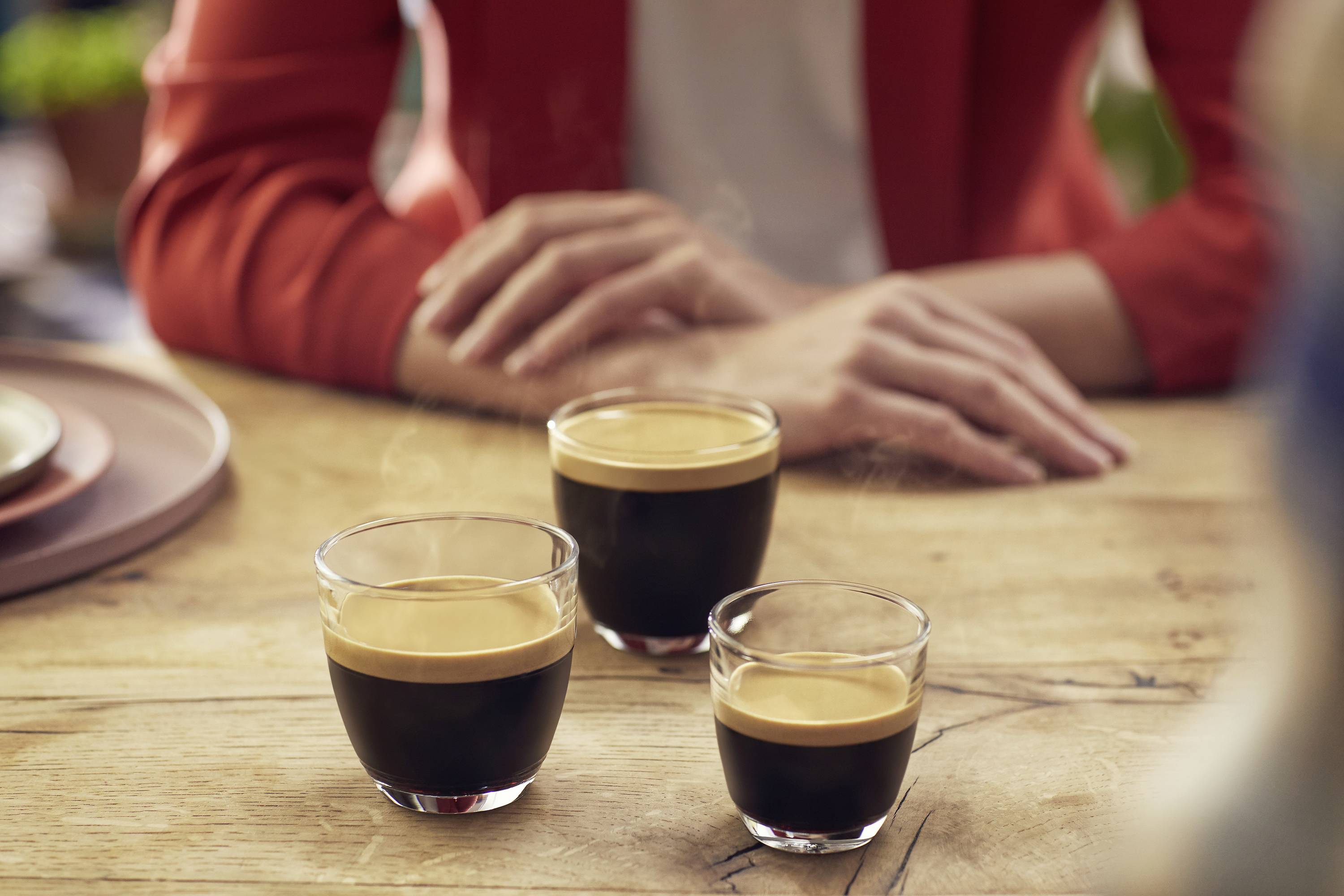 A person is sitting at a table with three espresso glasses in front of them. The scene conveys a relaxed atmosphere in a café.