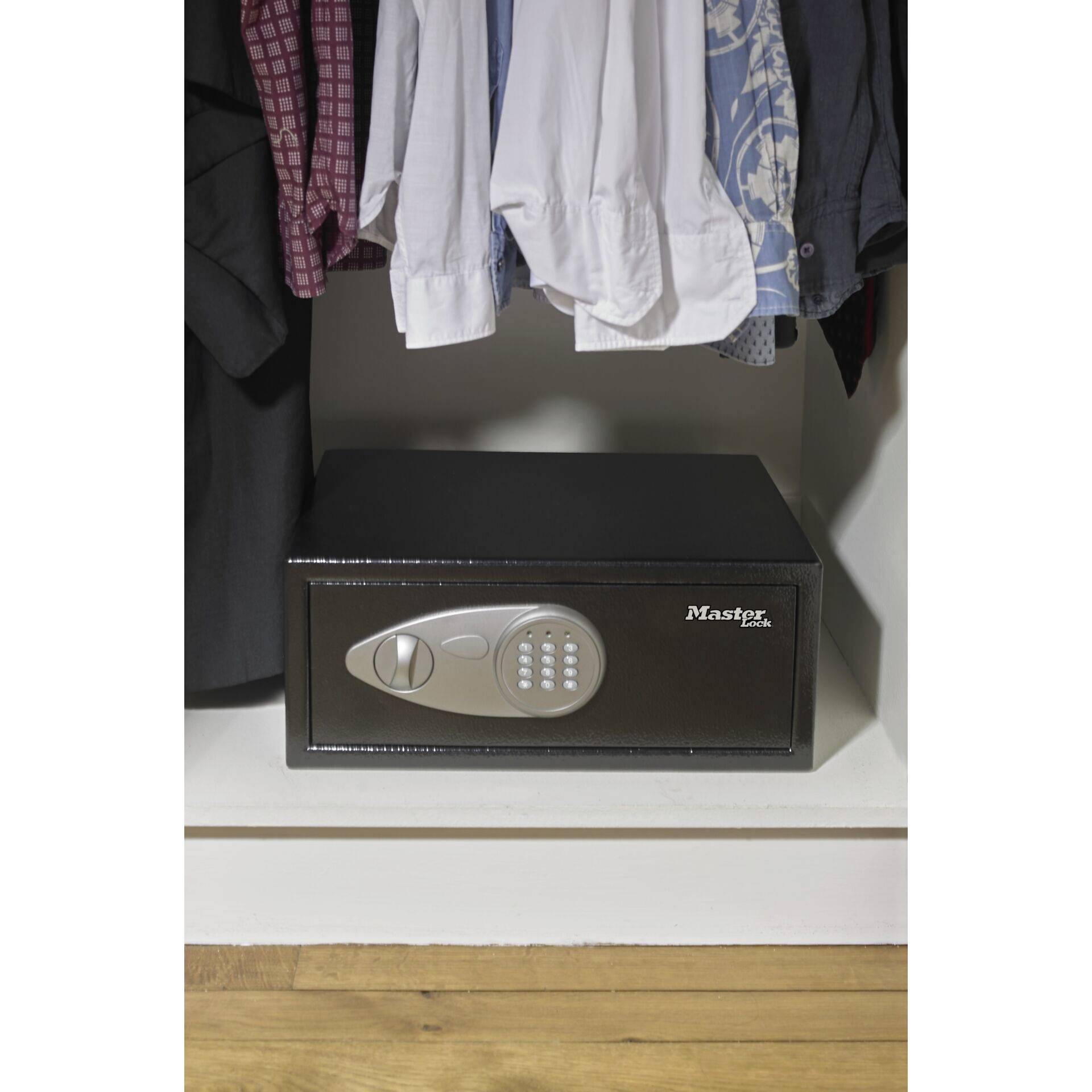 A safe with a numerical keypad is located in a cupboard beneath hanging clothes.
