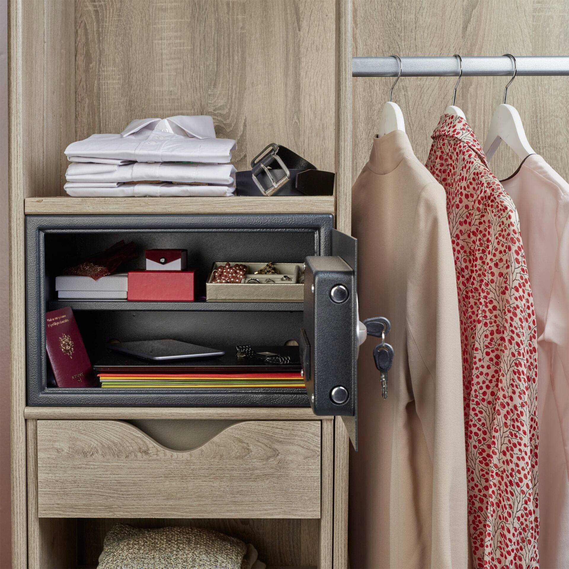 Open safe inside a wooden cabinet with documents and jewellery inside; clothing items hanging on coat hangers beside it.