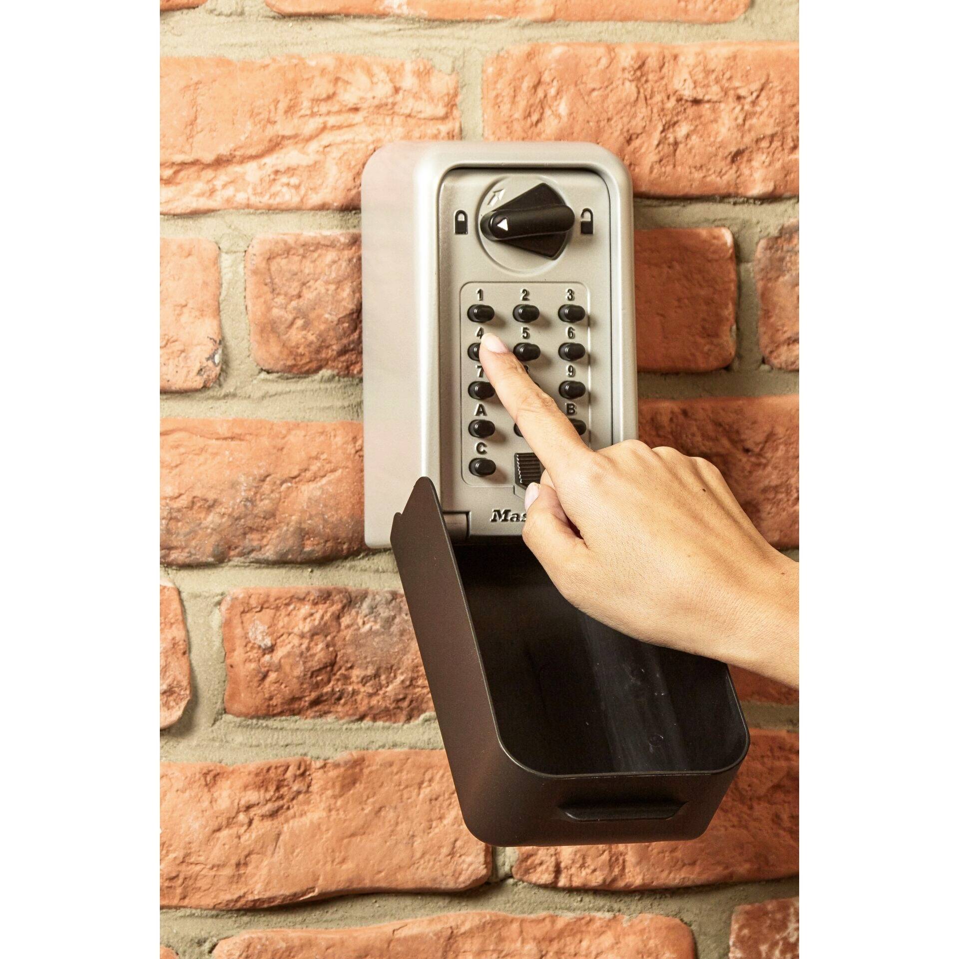 A finger points at the keys of a security code lock mounted on a brick wall.