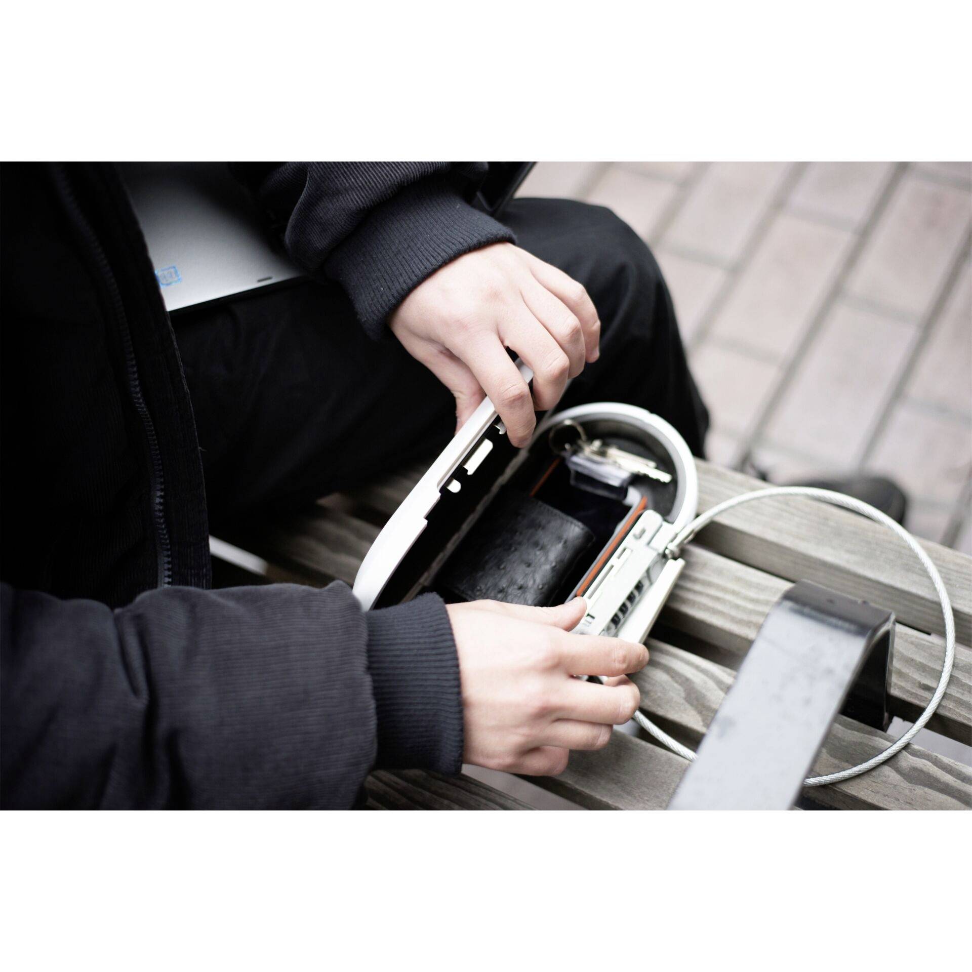 A person is sitting on a bench and holding an open padlock with a cable.