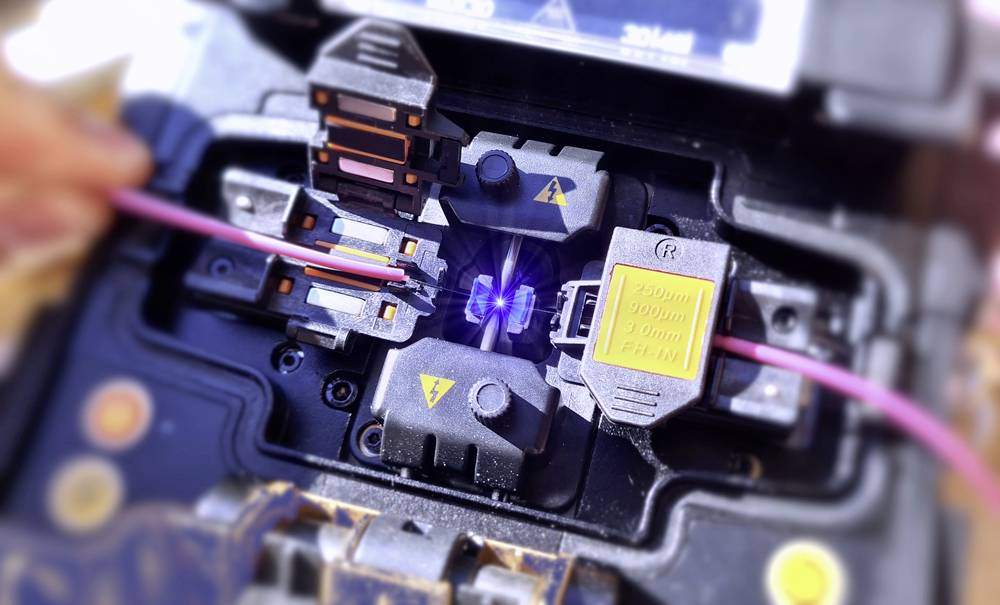 Fibre optic splicing machine in action, showing the process of fusion-joining optical fibre cables with an electric arc between the fibres.